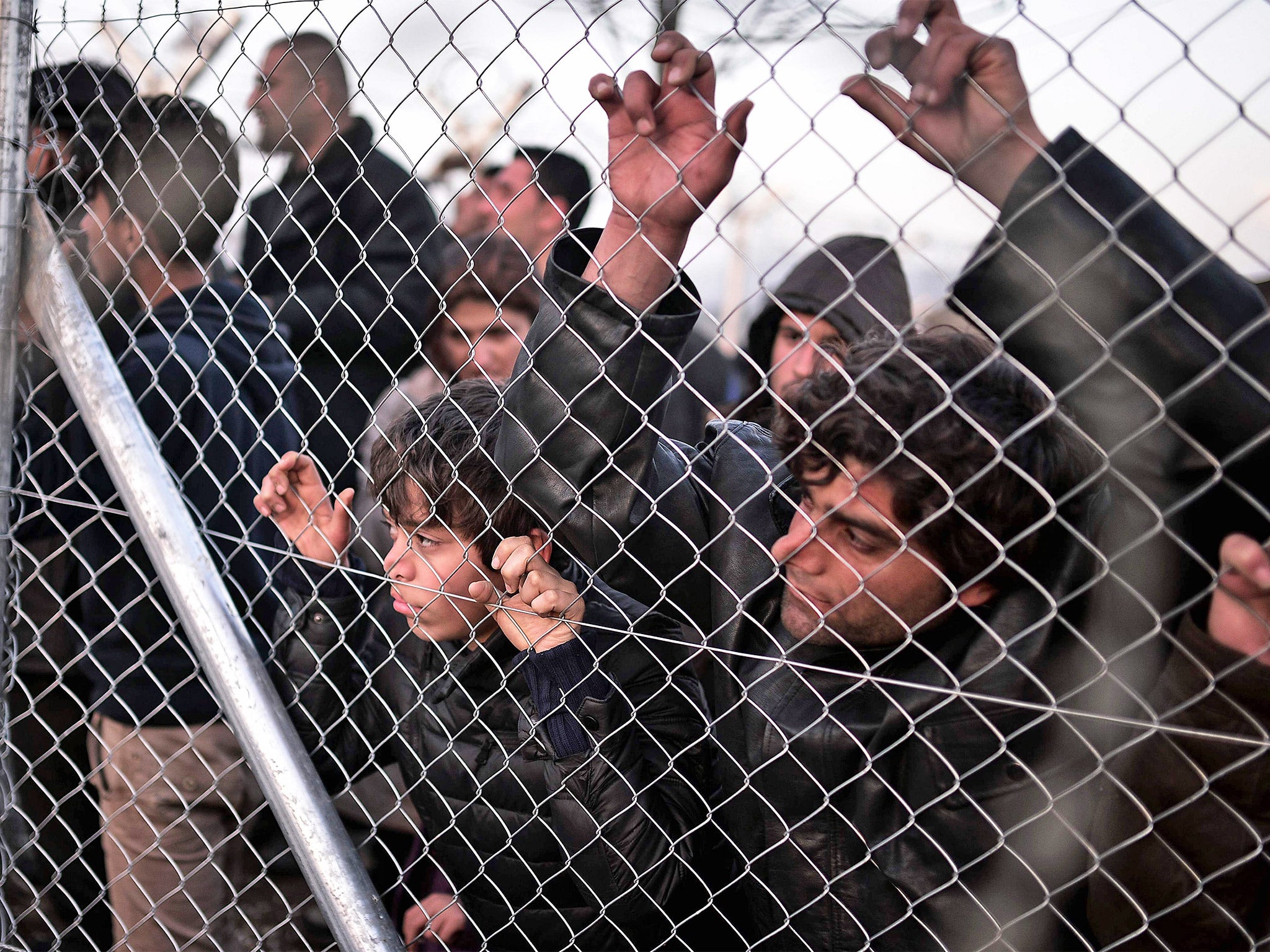 Refugees look through a fence at the Greek-Macedonian border