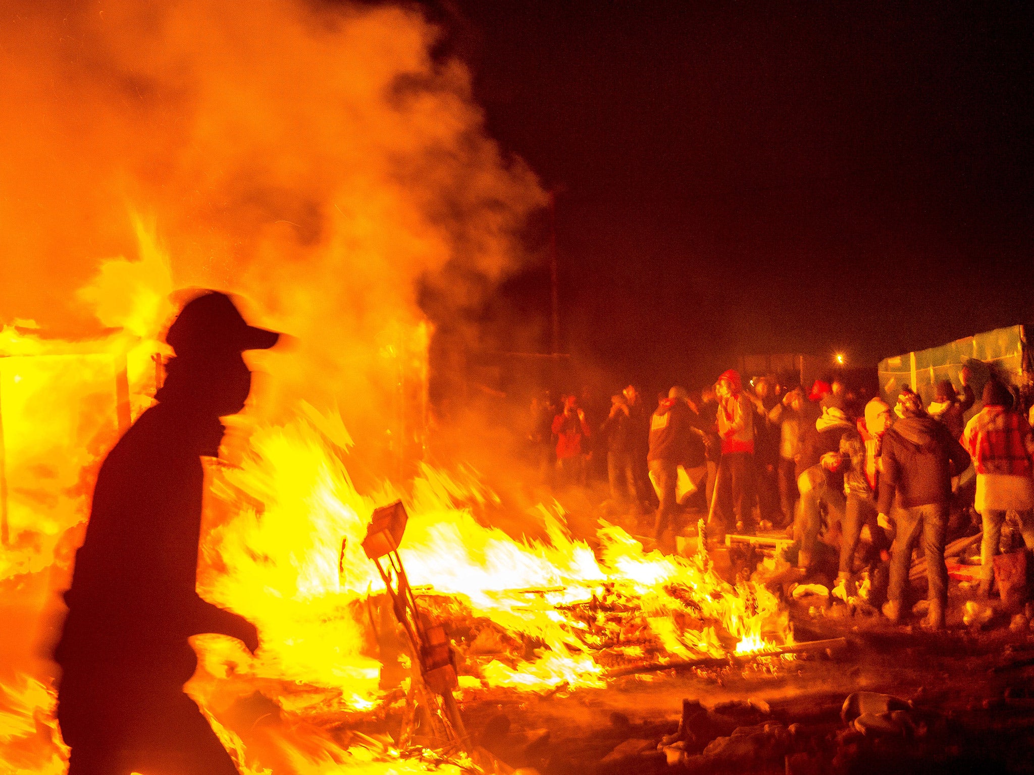 Refugees watch on as shacks are burnt down at the Jungle camp in Calais