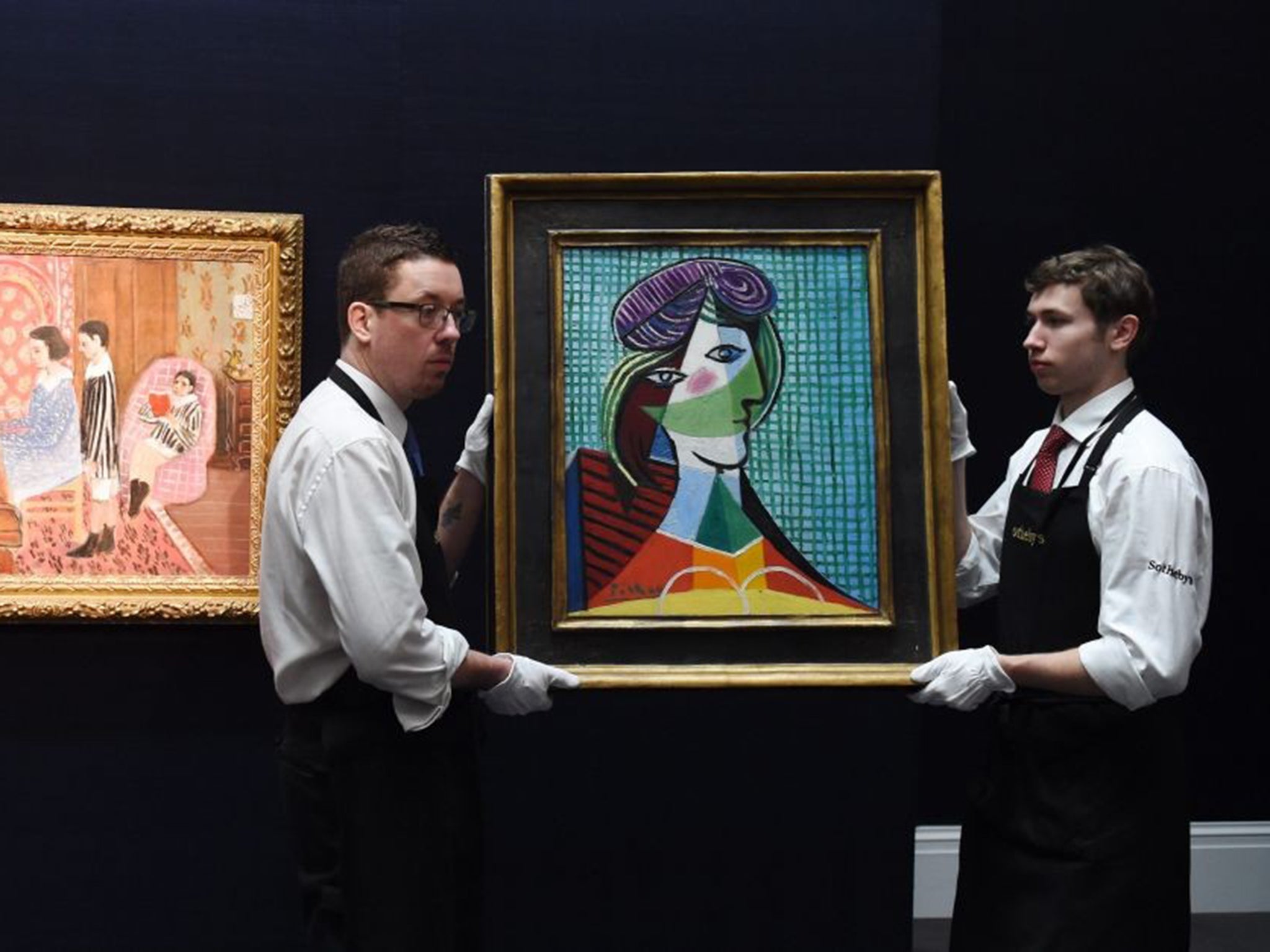 Staff members carry the painting 'Tete de Femme (1935)' by Spanish artist Pablo Piccaso next to French artist Henri Matisse's work 'La Lecon de Piano' during a press preview at Sotheby's auction house in London