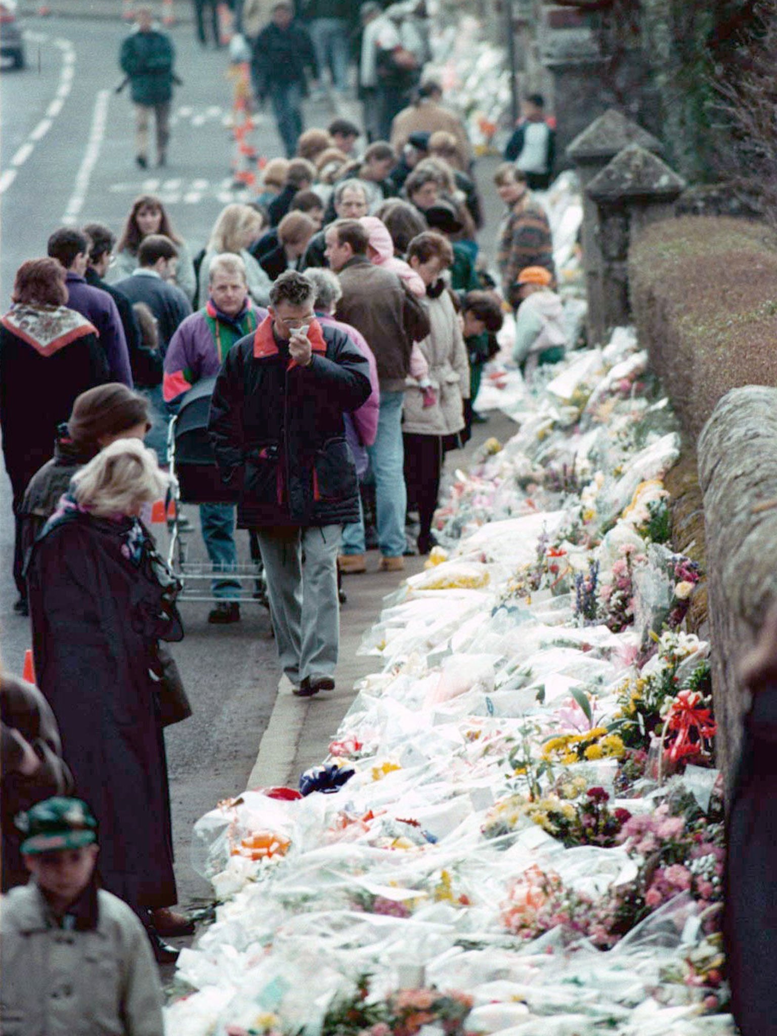 People looking at floral tributes lining the road by Dunblane Primary School three days after the shooting in which 16 pupils and their teacher were killed.