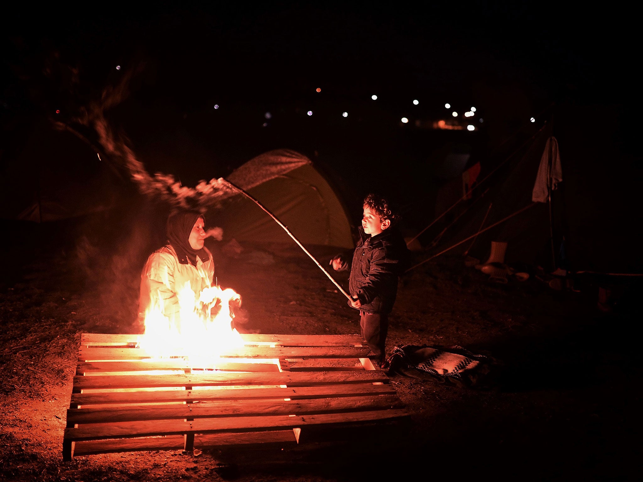 A boy plays with a stick by a bonfire at the makeshift refugee camp near the village of Idomeni, where thousands of migrants and refugees are stranded