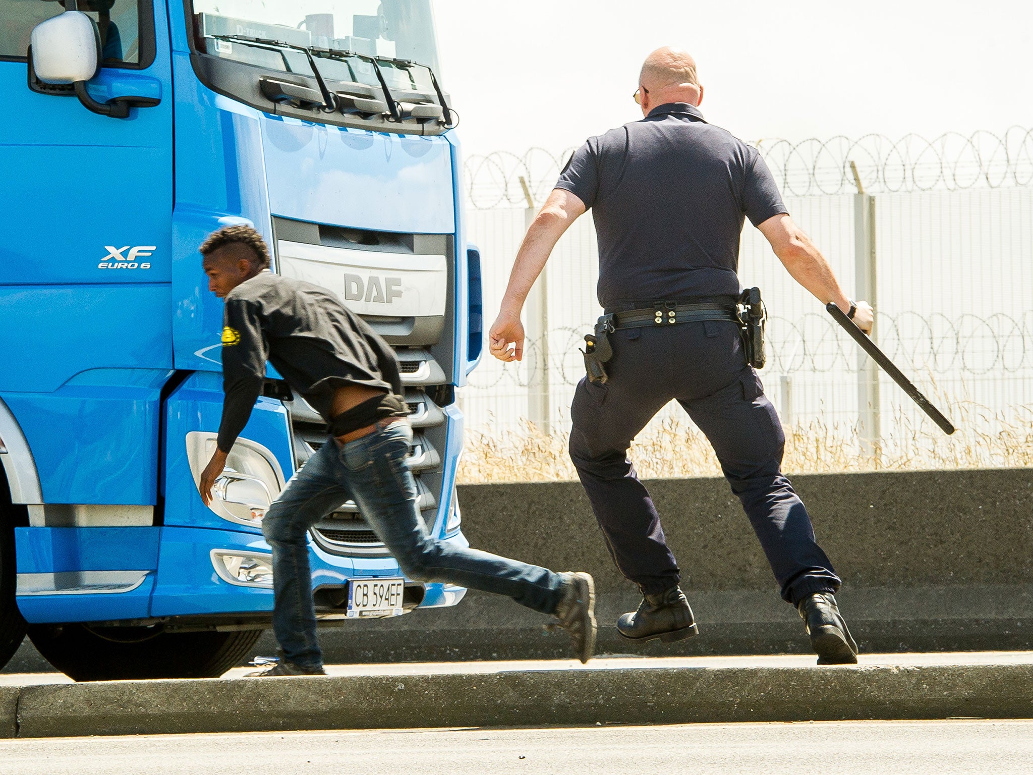 French police (CRS) officer runs after a migrant trying to hide in a lorry heading for England in Calais