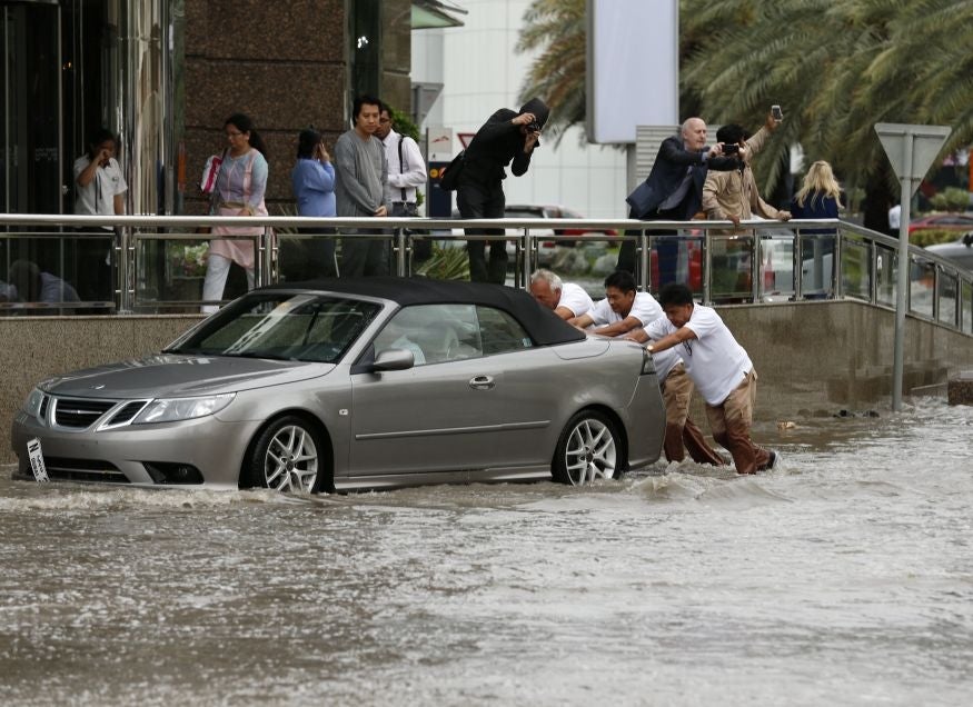 Men are seen pushing a car through a flooded street in Dubai