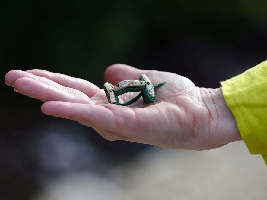 MAP Archaeological Practice staff member Sophie Coy holds a bronze brooch with a coral enamel, which was found at the site