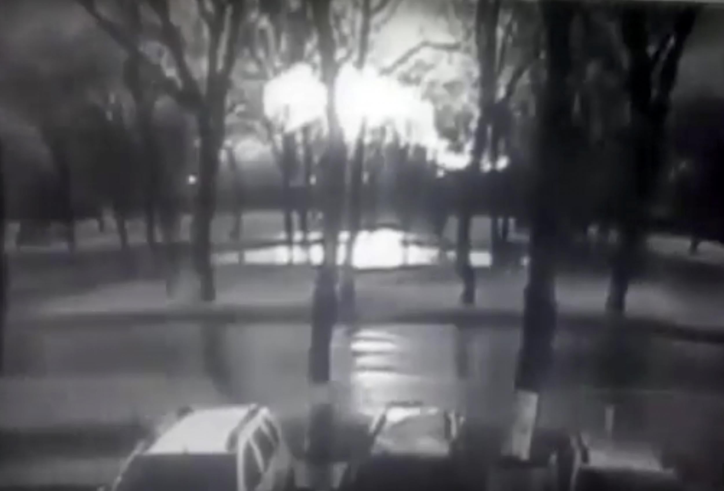 Black and white CCTV footage shows road and behind line of trees fireball, believed to be the plane on fire