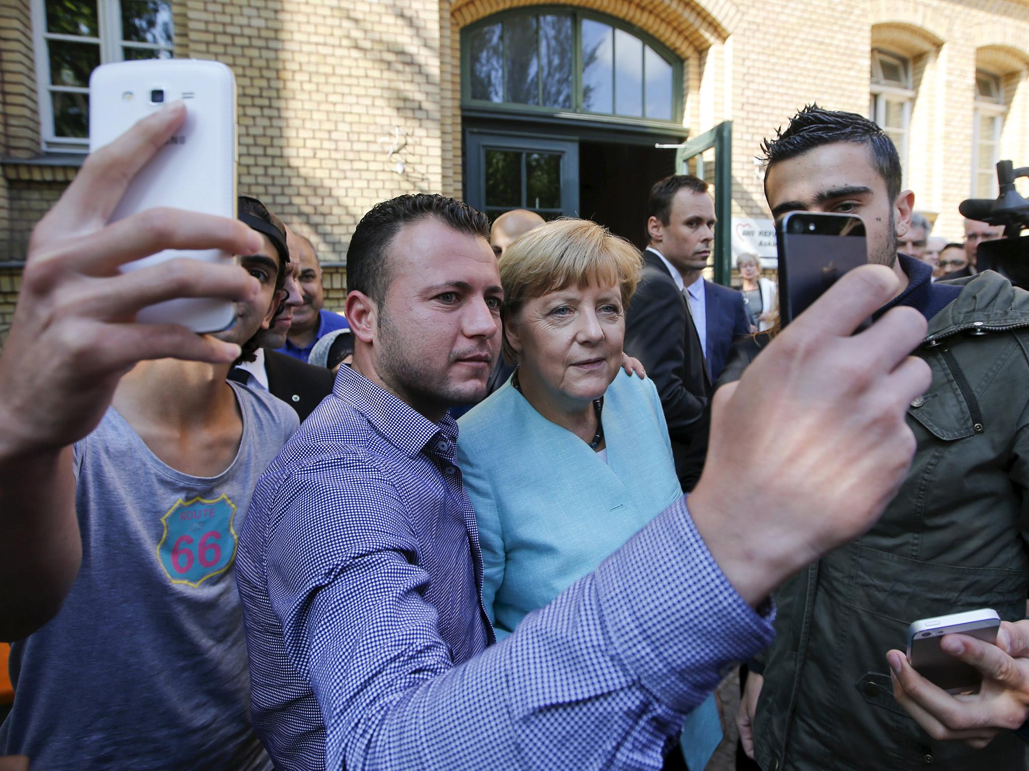 Migrants from Syria and Iraq take selfies with German Chancellor Angela Merkel outside a refugee camp near the Federal Office for Migration and Refugees after their registration at Berlin's Spandau district, Germany