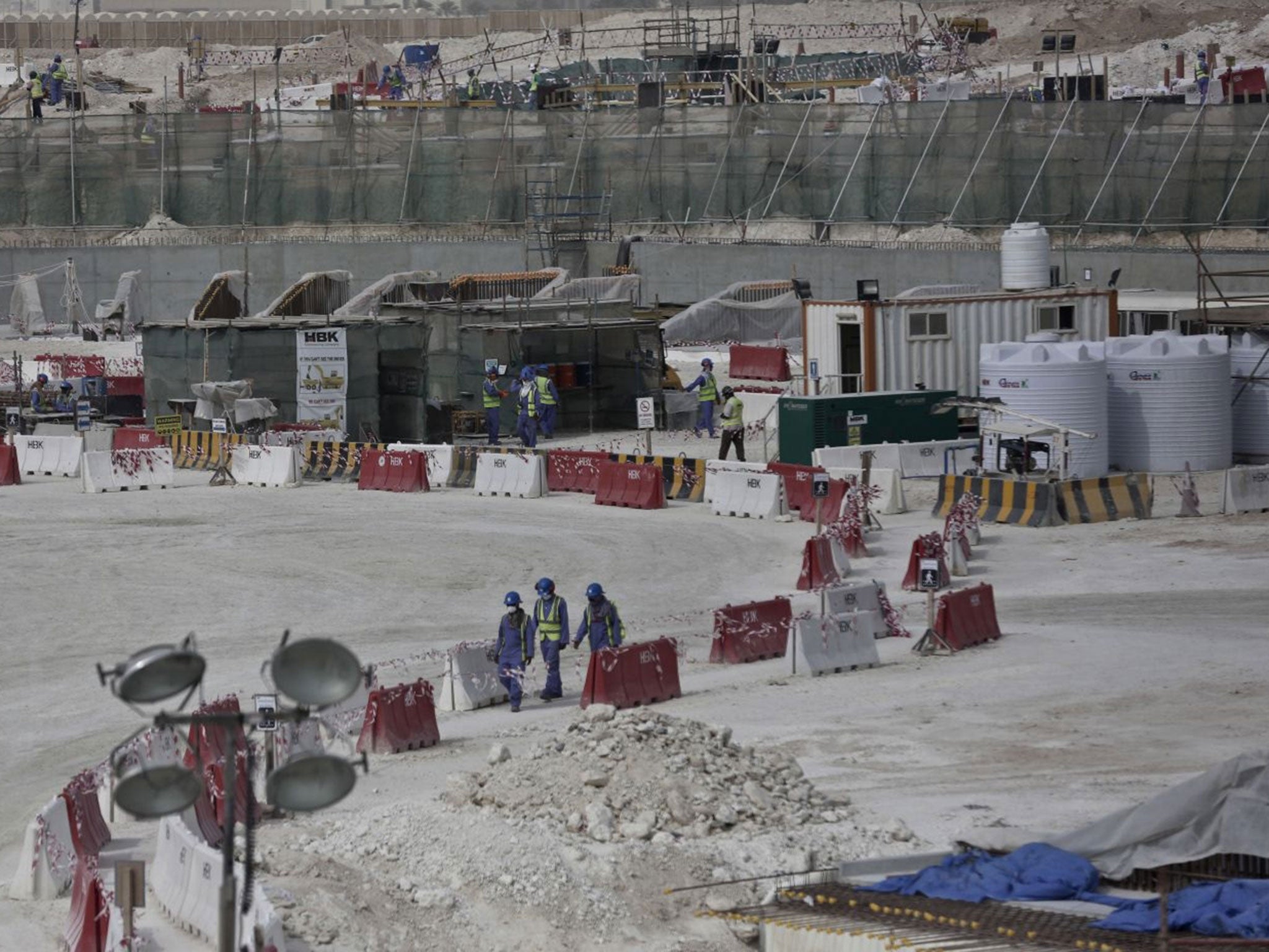 In this 4 May, 2015, file photo taken during a government organized media tour, foreign workers walk between safety barricades at the site of the pitch of the Al-Wakra Stadium that is under construction for the 2022 World Cup in Doha, Qatar