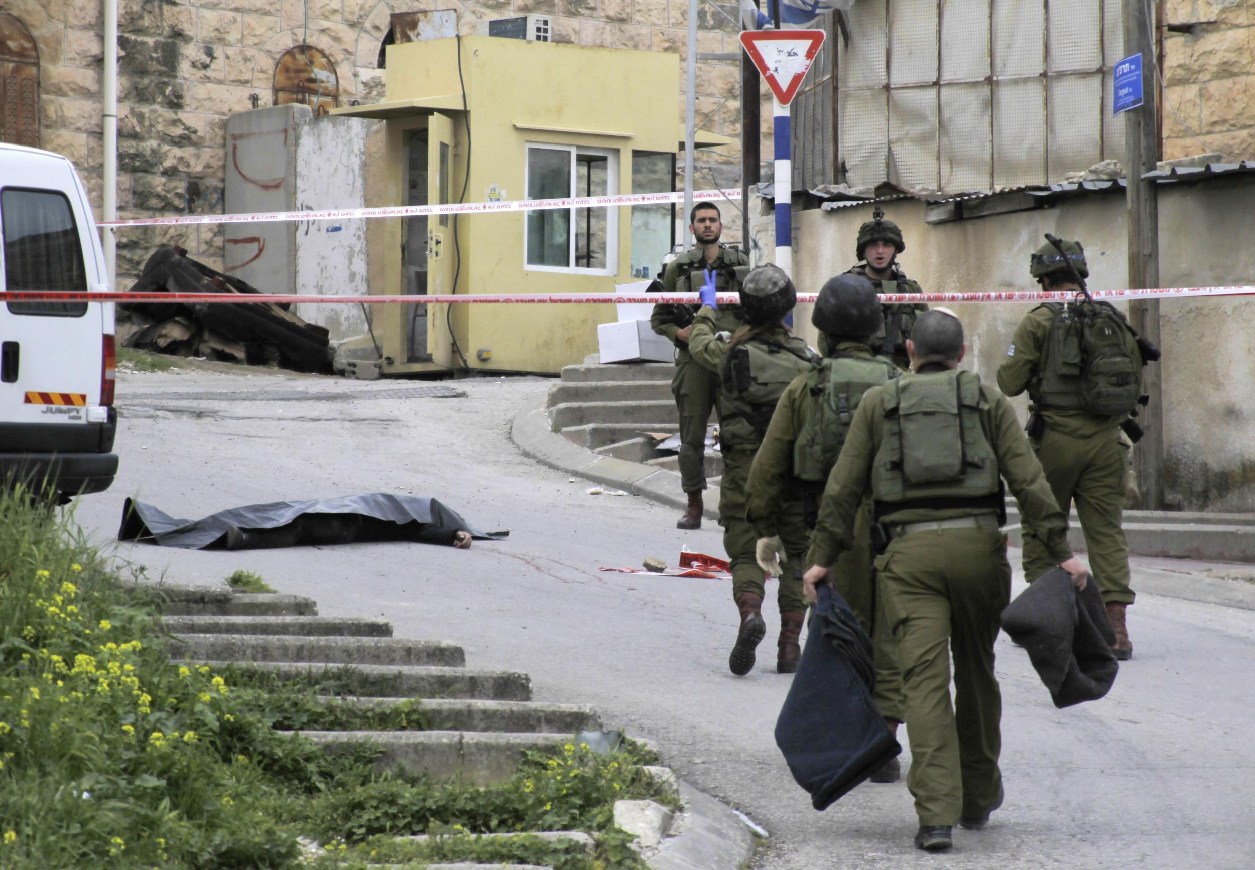 Israeli soldiers attend the body of Abed al-Fatah al-Sharif, who was shot and killed by a soldier while laying wounded on the ground in Hebron