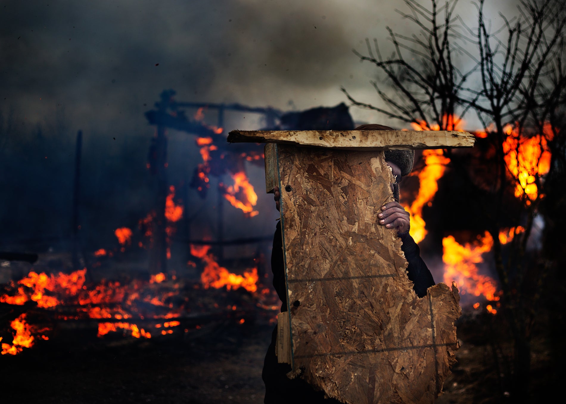 A man salvages wood from a burning home in the south side of the Calais camp (Photo: Emily Garthwaite)