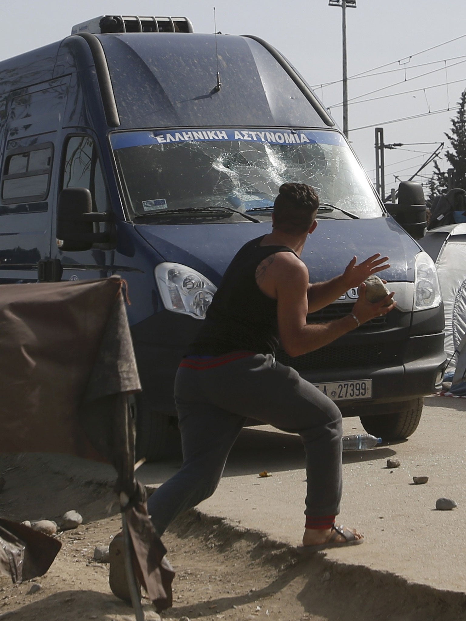 A migrant throws a stone at a police car after clashes at a makeshift camp for migrants and refugees at the Greek-Macedonian border near the village of Idomeni, Greece, April 18, 2016.