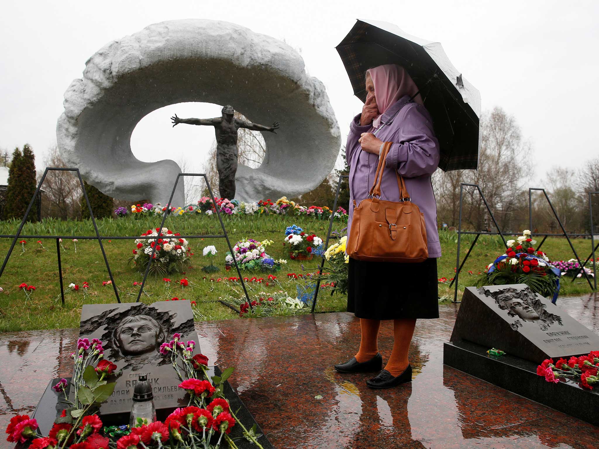 A woman stands near the grave of her brother, a "liquidator" or an emergency worker who fought the blaze at the Chernobyl nuclear reactor, during a commemoration ceremony on the 30th anniversary of the Chernobyl nuclear disaster at the Mitino cemetery in Moscow