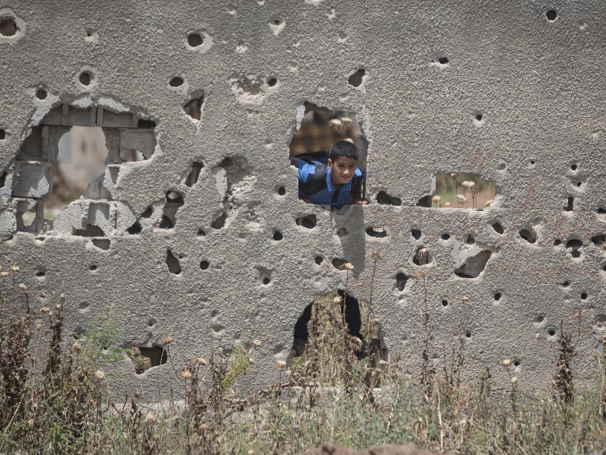 &#13;
A Palestinian boy stands behind a wall in Gaza City damaged during the 50-day war between Israel and Hamas-led militants in the summer of 2014 (Getty)&#13;