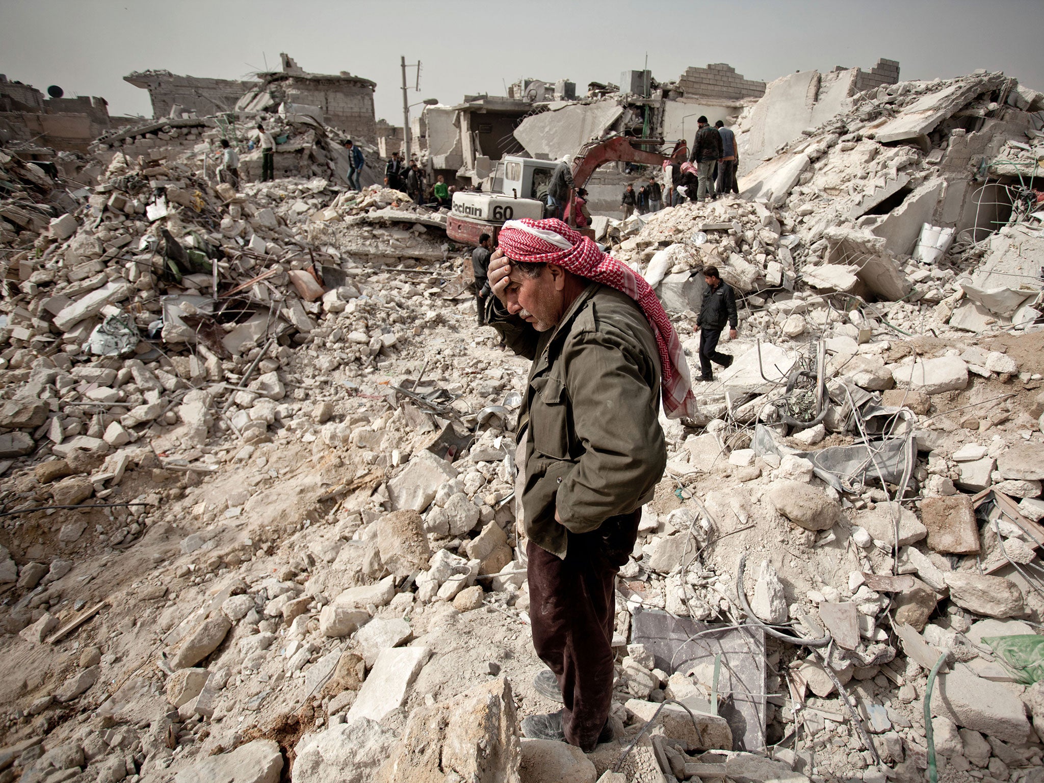 A Syrian man reacts while standing on the rubble of his house while others look for survivors and bodies in the Tariq al-Bab district of the northern city of Aleppo on 23 February, 2013