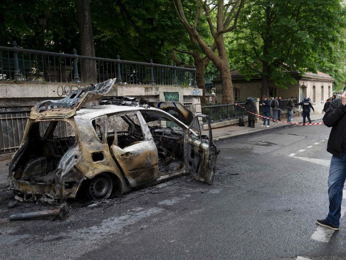 Police officers stand guard next to a burned-out police car