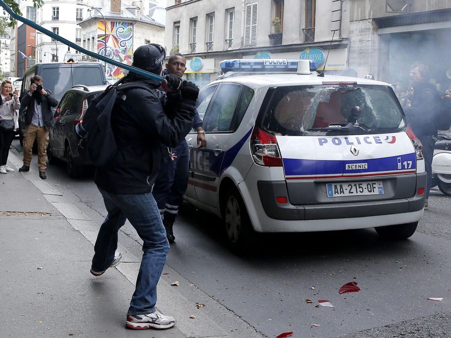 A protester hits a policeman with a bar after attacking a police car during a demonstration