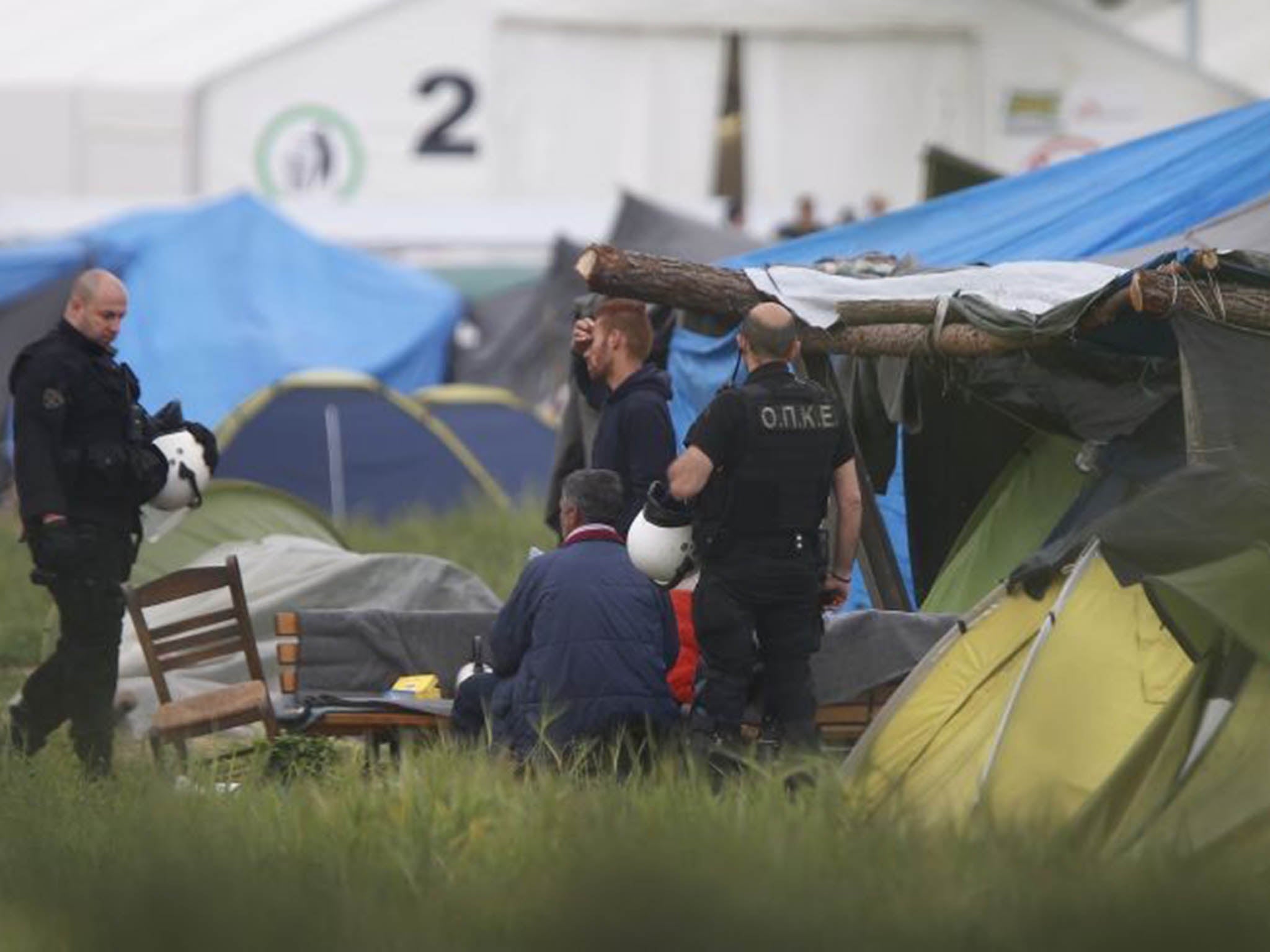 Greek policemen stand next to migrants at a makeshift refugee camp at the Greek-Macedonian border