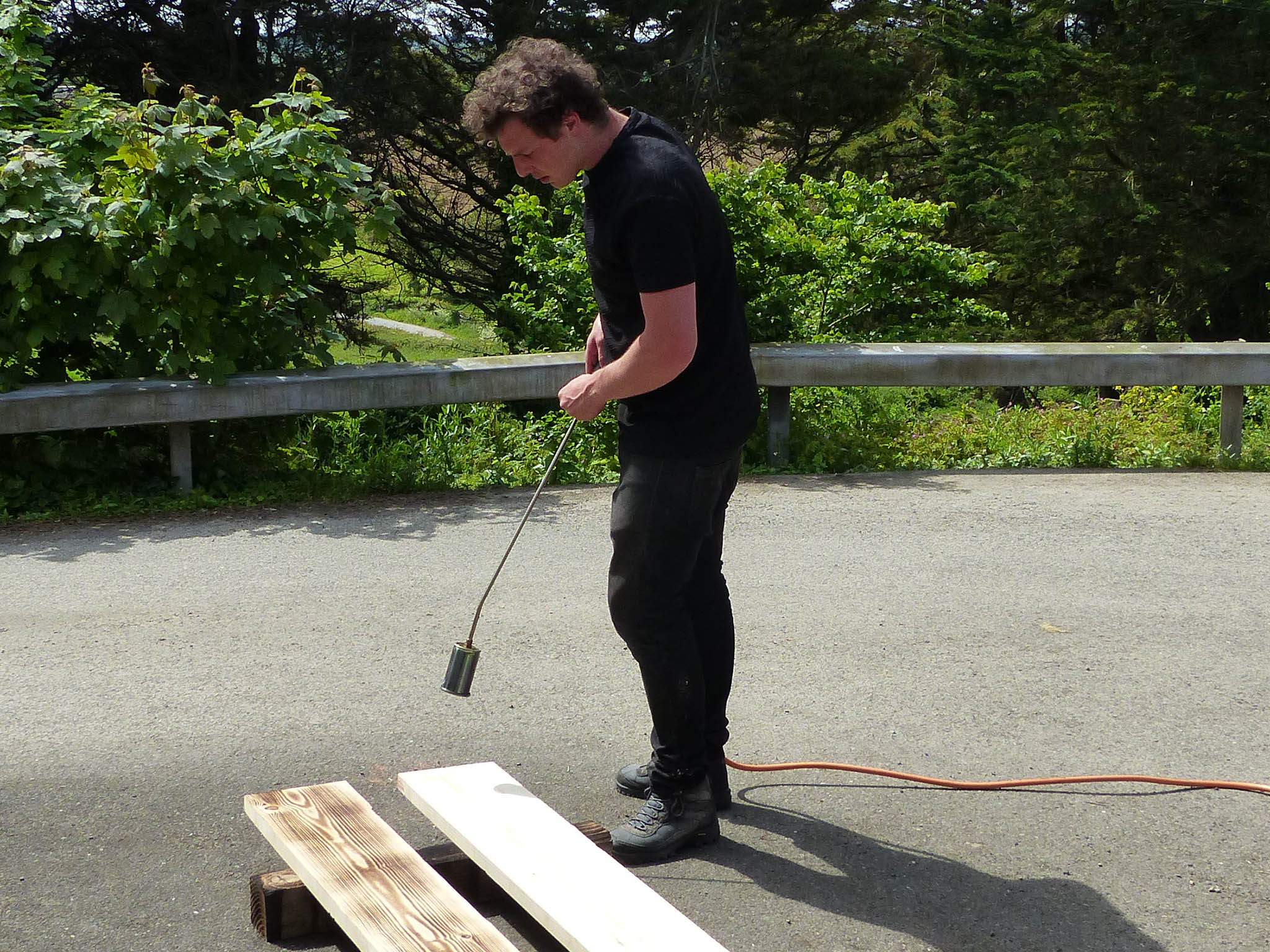 Max uses a blow torch to burn the wood outside his workshop