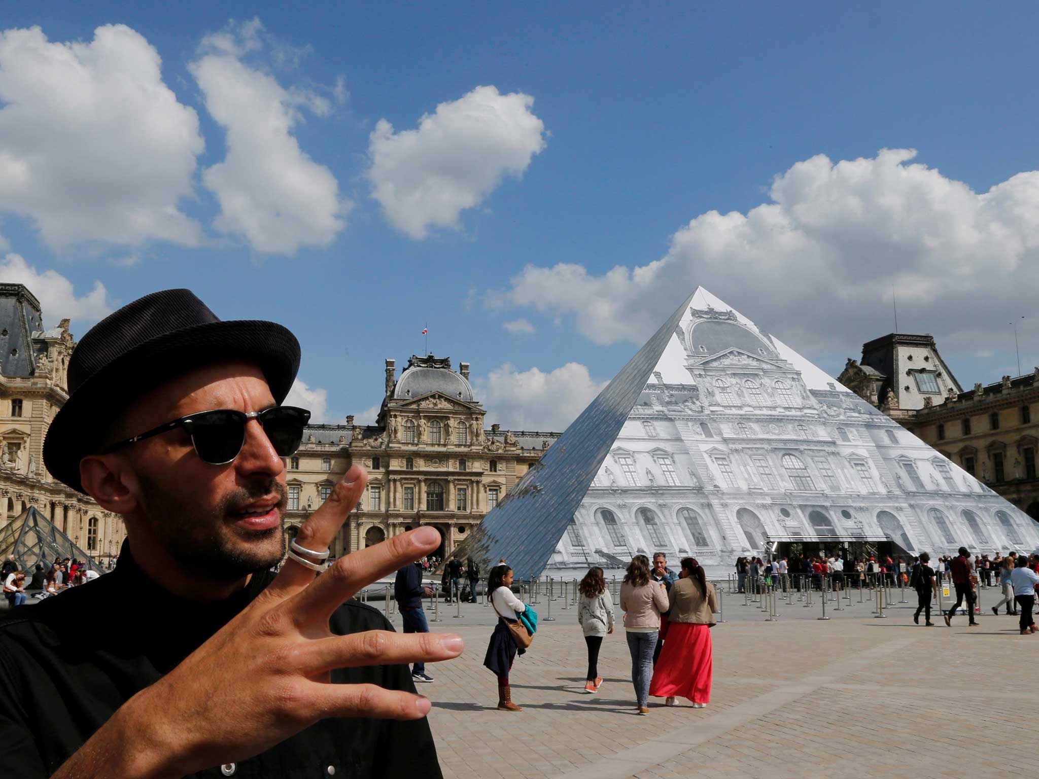 French artist JR stands in front of his latest work, an image of the facade of Paris' Louvre covering the museum's pyramid entrance