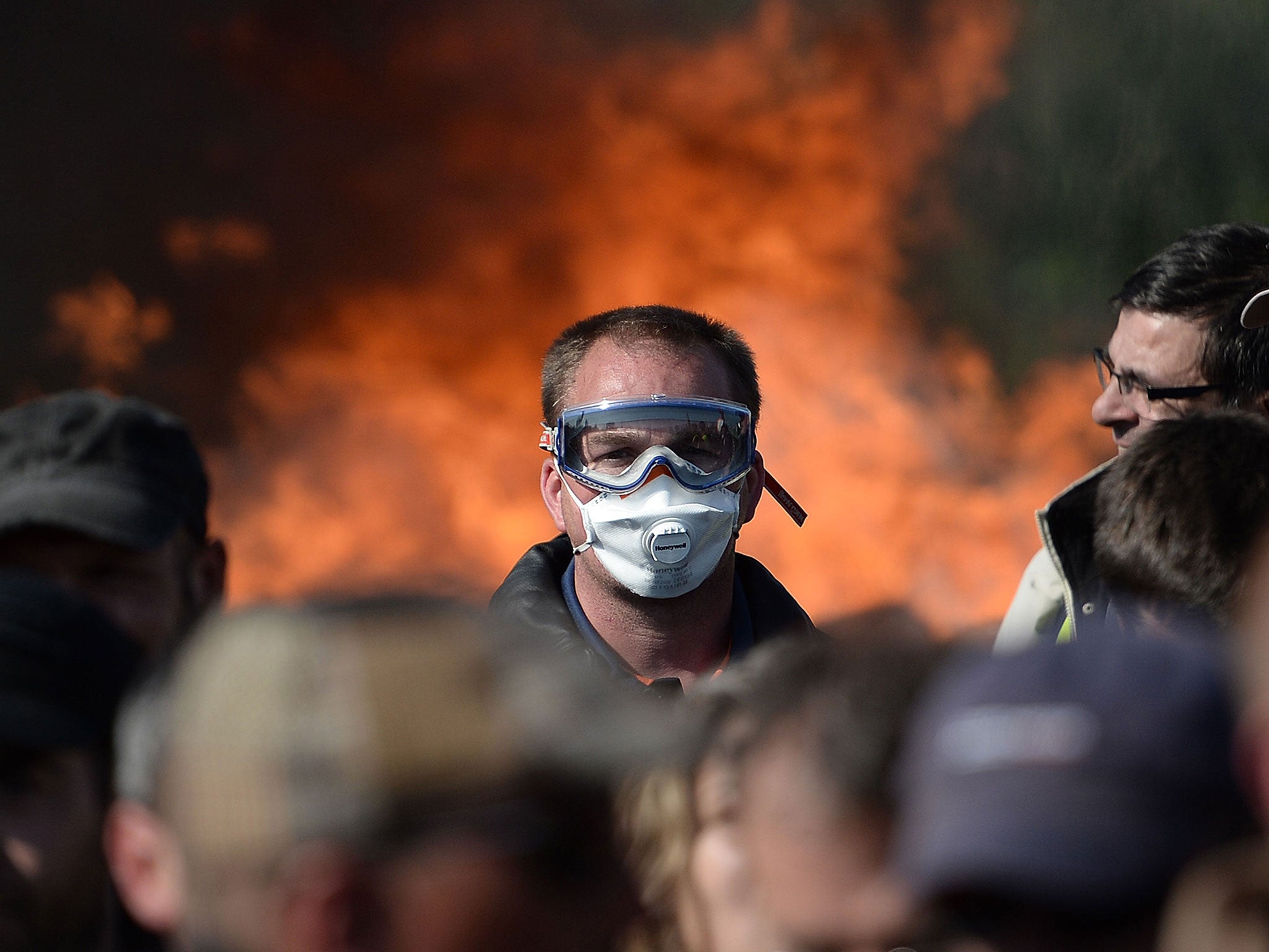 A man with a mask is pictured as workers on strike are evacuated by riot policemen as they block the access to an oil depot near the Total refinery of Donges, western france, on May 27, 2016 to protest against the government's planned labour law reforms