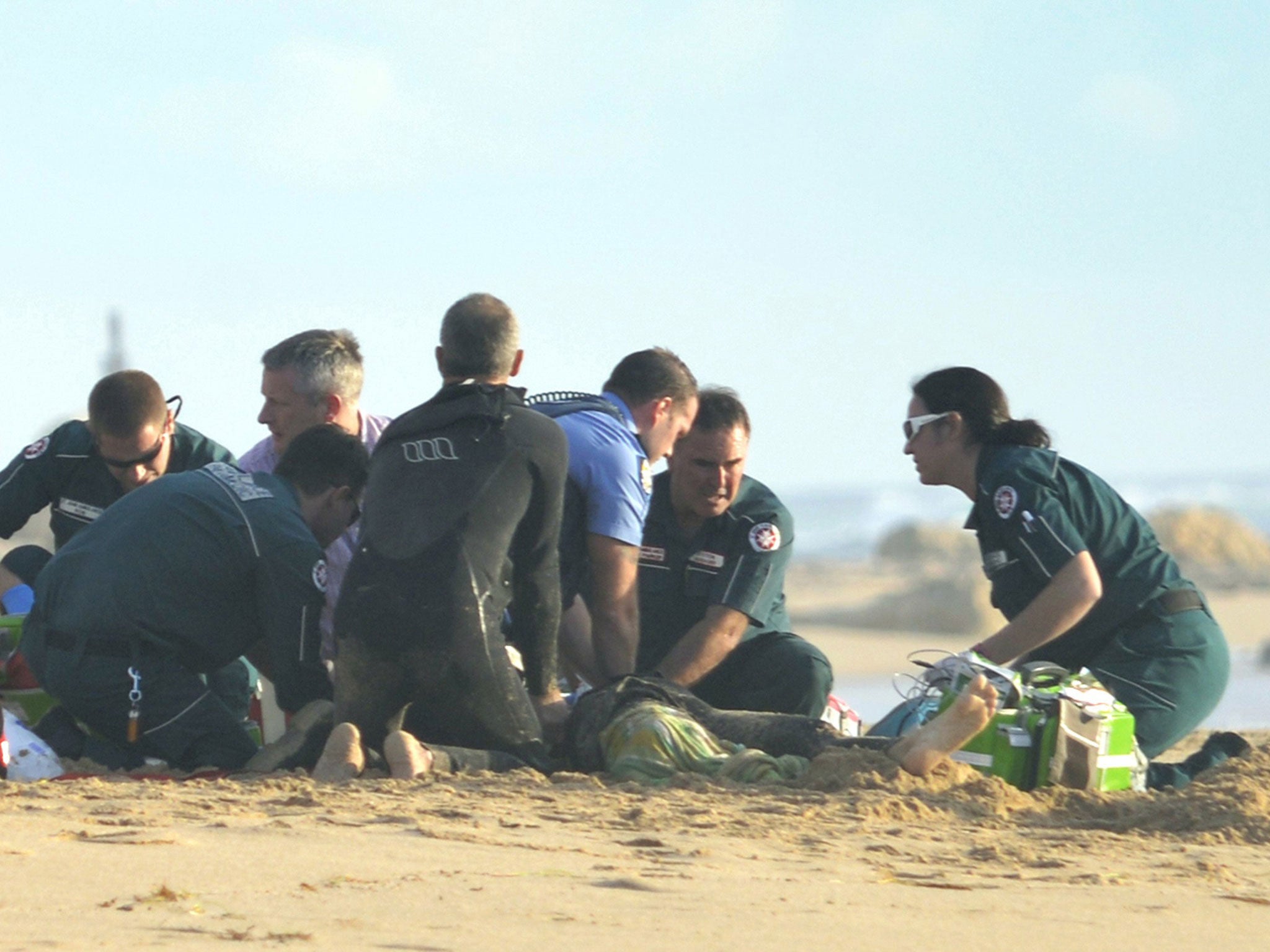 Ambulance and police officers help a critically injured surfer after a shark ripped off his leg in an attack in Western Australia