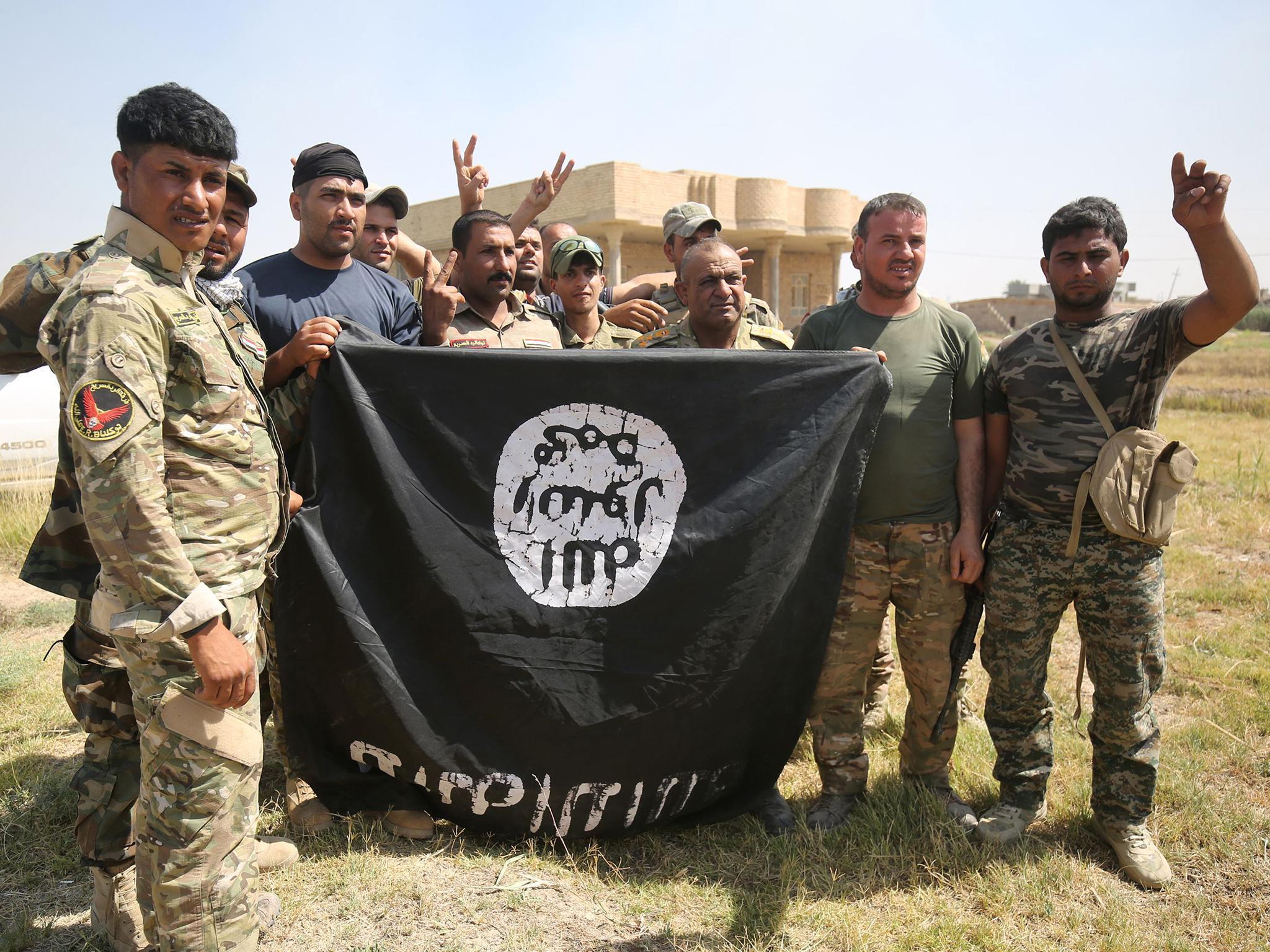 Shia fighters hold an Isis flag in an operation east of Fallujah – the terror group has lost ground in both Syria and Iraq (AFP/Getty Images)