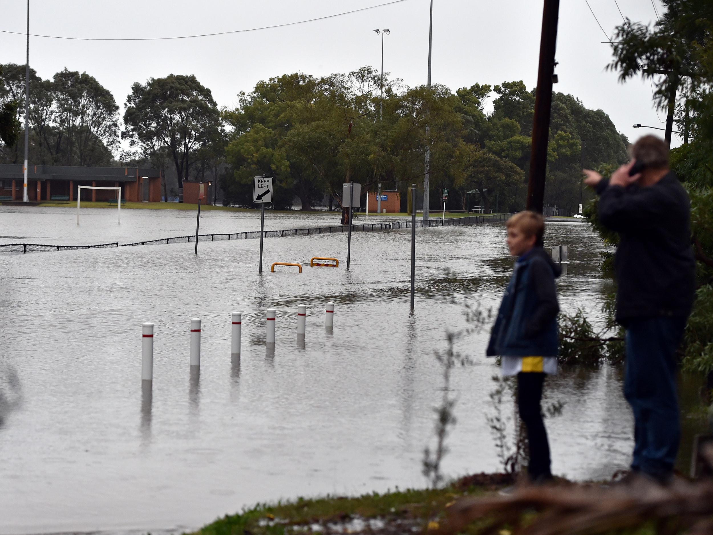 Residents wait at the end of a flooded road after the Georges River burst its banks in Sydney