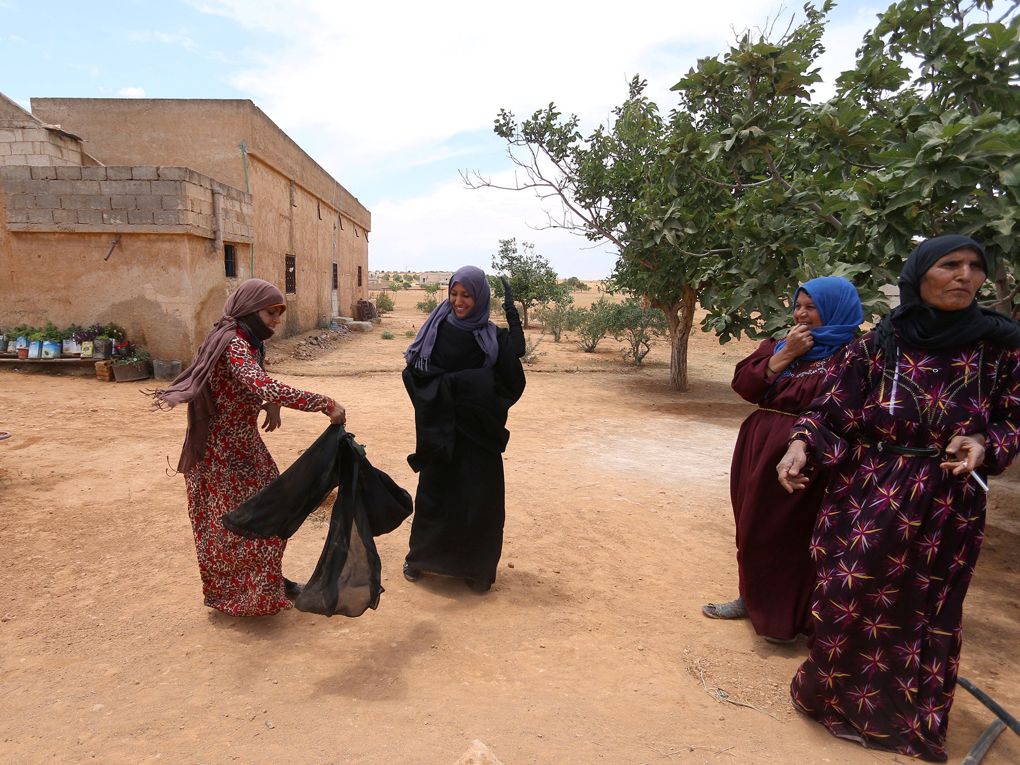 A woman removes her Niquab to reveal a floral dress and purple headscarf