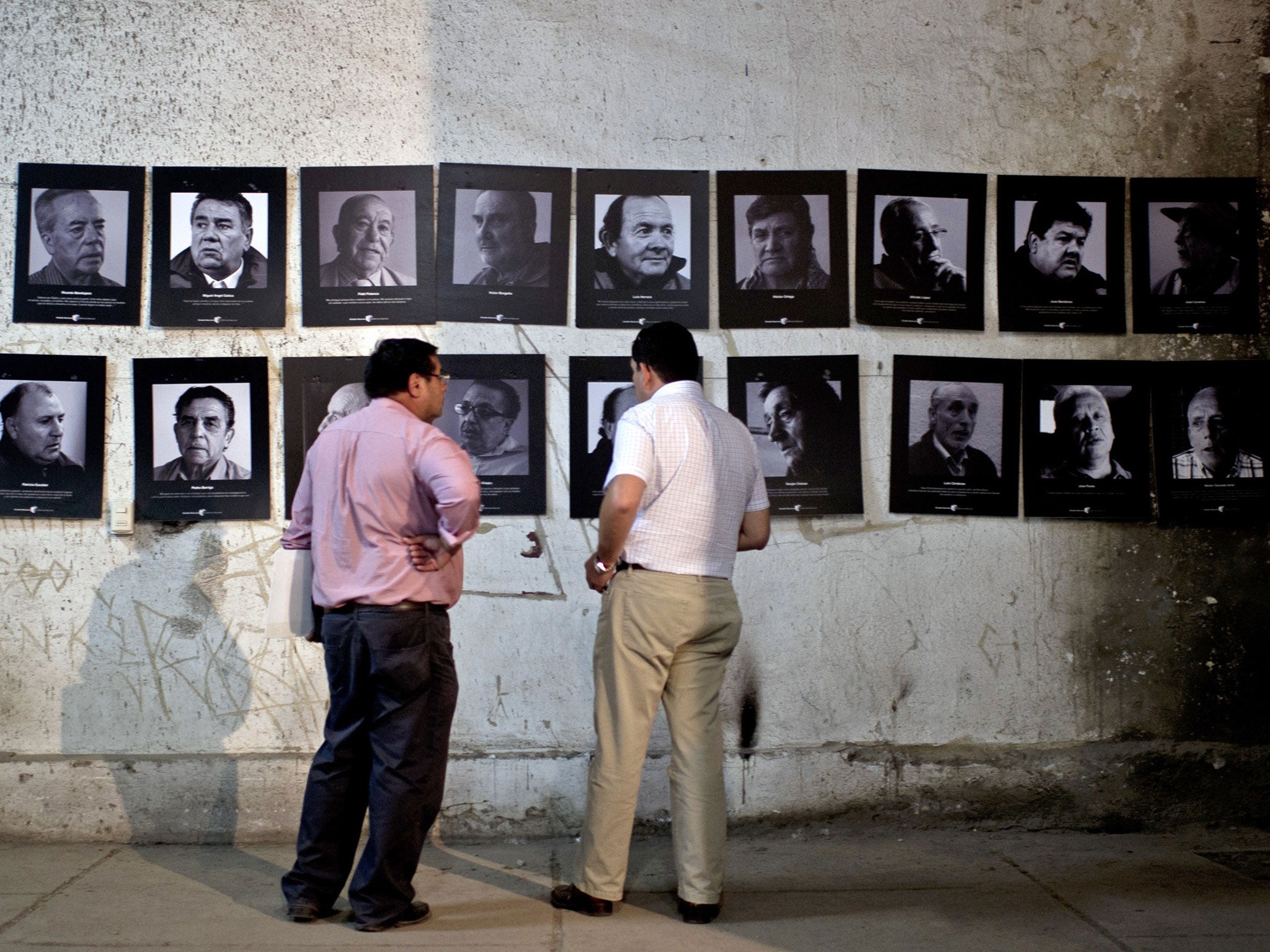 Members of the 'Former Political Prisoners of the National Stadium' stand next to pictures in a room at the National Stadium that served as a jail for prisoners during the killings