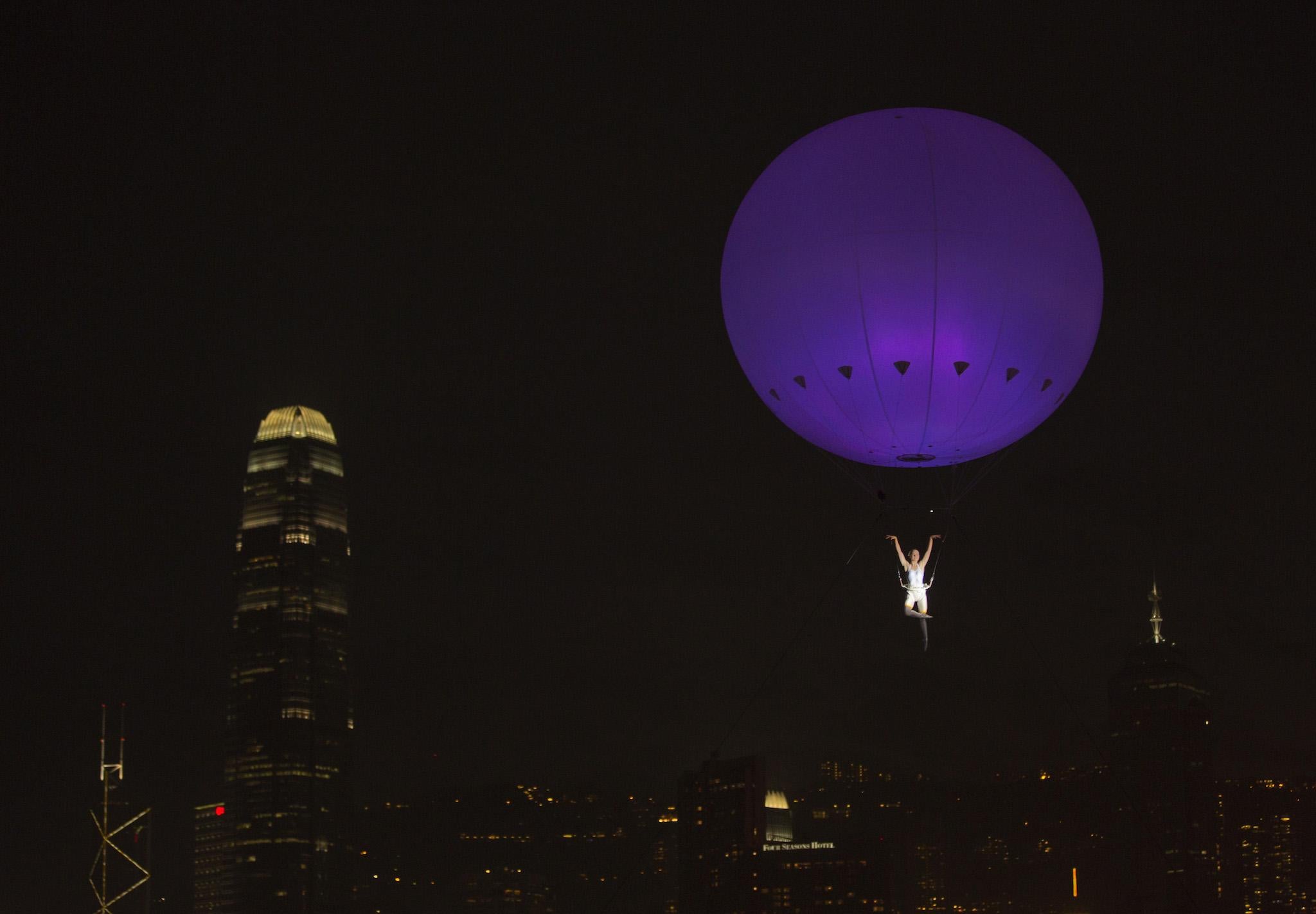 A dancer of London's the Dream Engine performs under the heliosphere, a massive helium balloon, with the backdrop of Hong Kong's skyline December 16, 2012