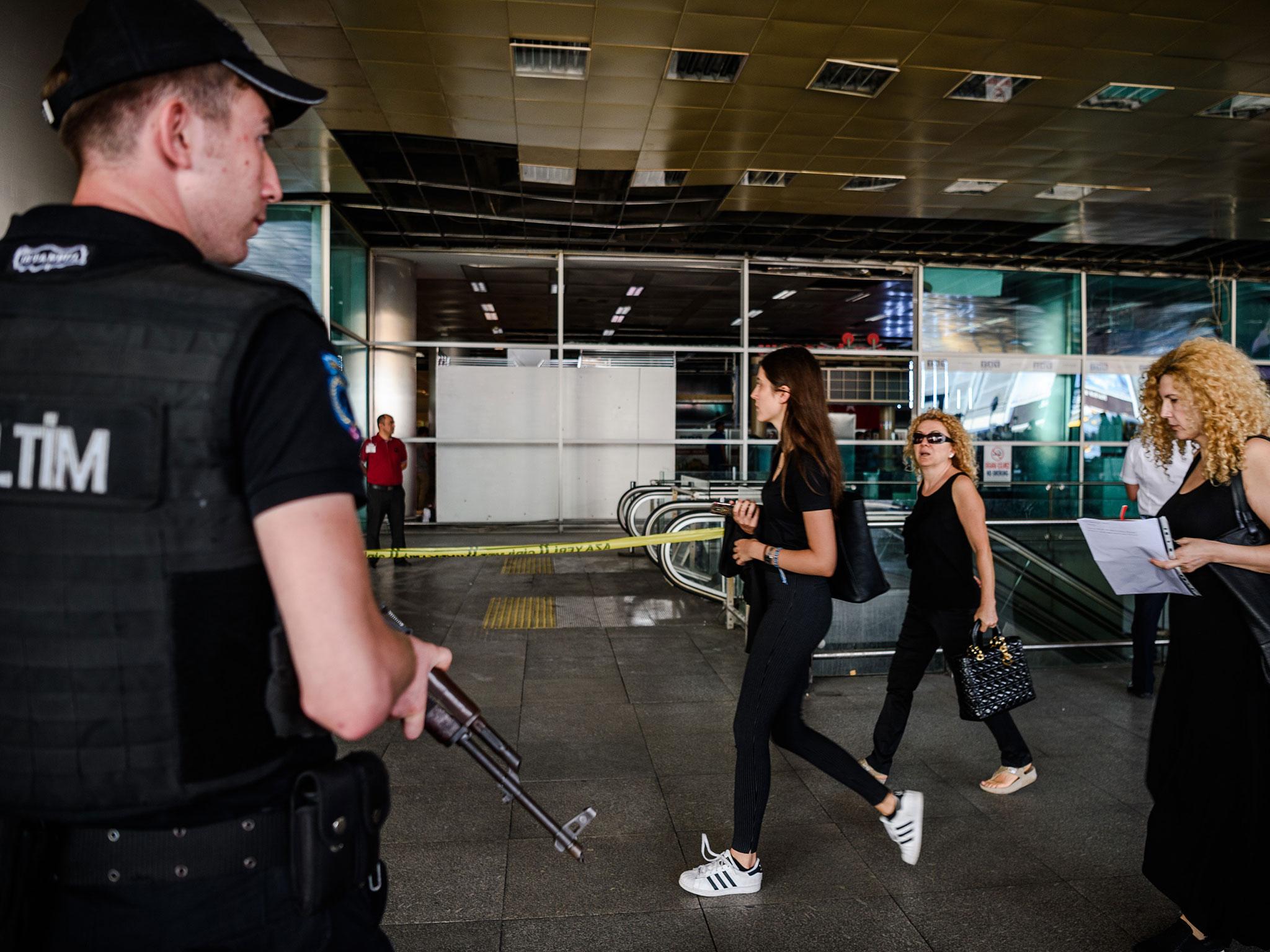 A Turkish anti-riot police officer stands guard as people walk past near the explosion site on 29 June, 2016 at Ataturk airport International arrival terminal in Istanbul, a day after a suicide bombing and gun attack targeted Istanbul's airport, killing at least 36 people