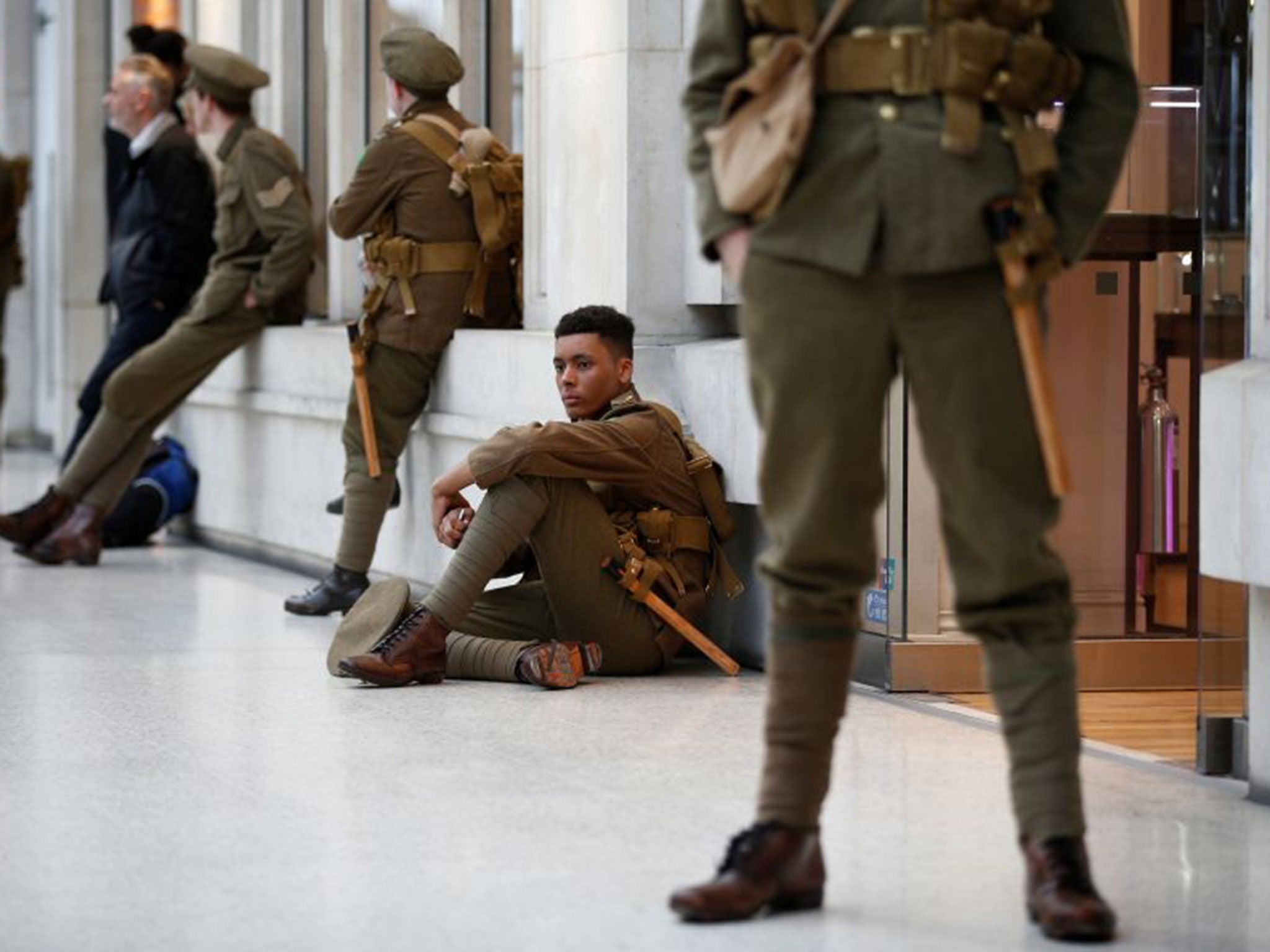 Volunteer actors dressed in World War I army fatigues stand silently in Waterloo station