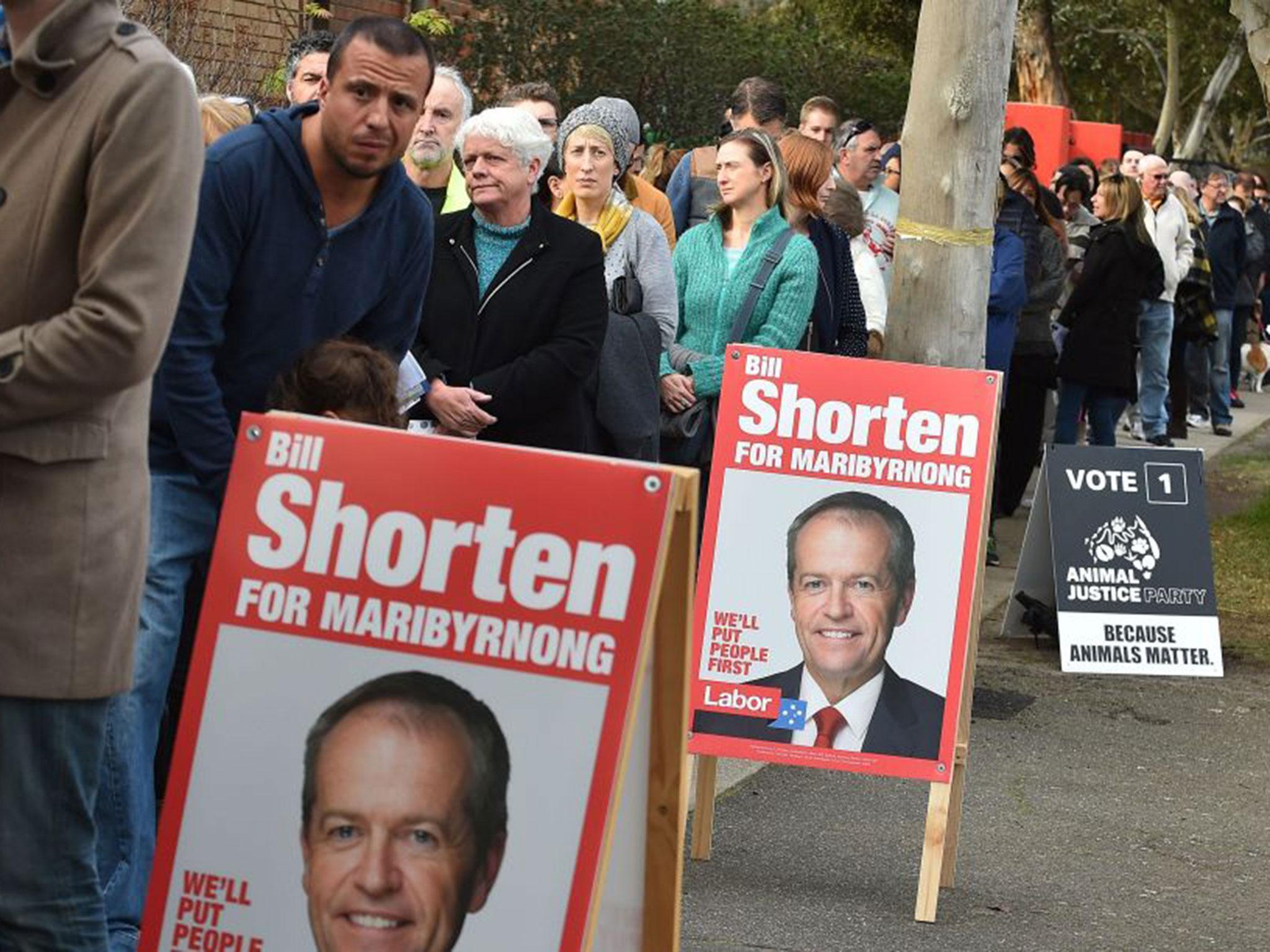 People wait in a queue next to posters of candidate Labor Party leader Bill Shorten, before casting their votes at a polling station in Melbourne
