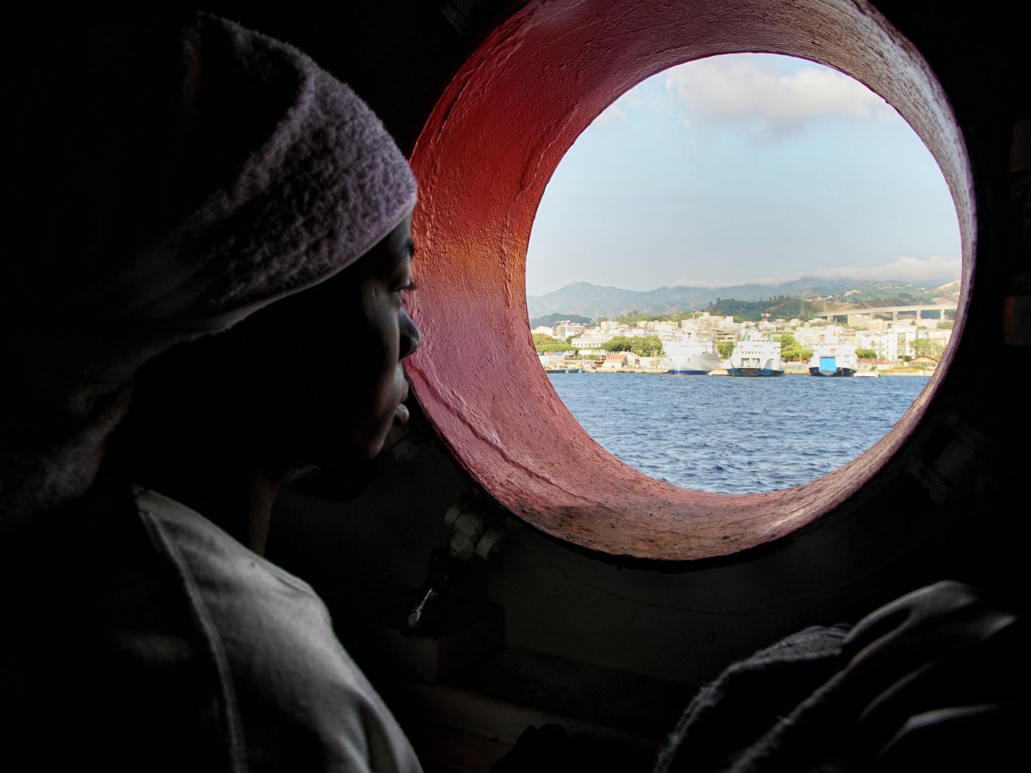 A woman looks out of the porthole from aboard the 'Aquarius' rescue vessel after arriving in Sicily, Italy, on Sunday June 25, 2016. A group of more than 650 migrants arrived at port in Messina, Sicily, after being rescued from the Mediterranean Sea in June 2016