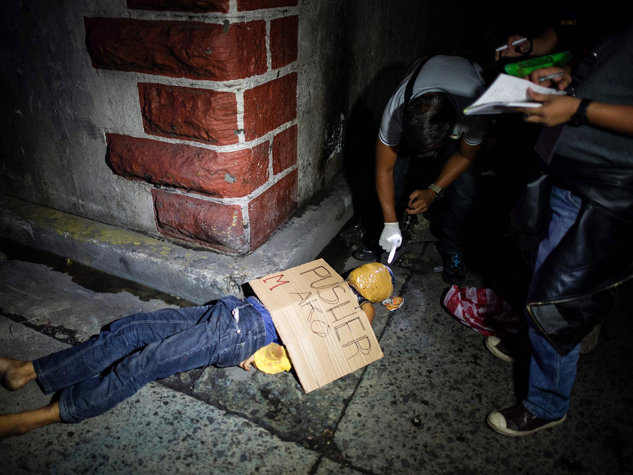 Police officers investigate the dead body of an alleged drug dealer, his face covered with packing tape on a street in Manila.