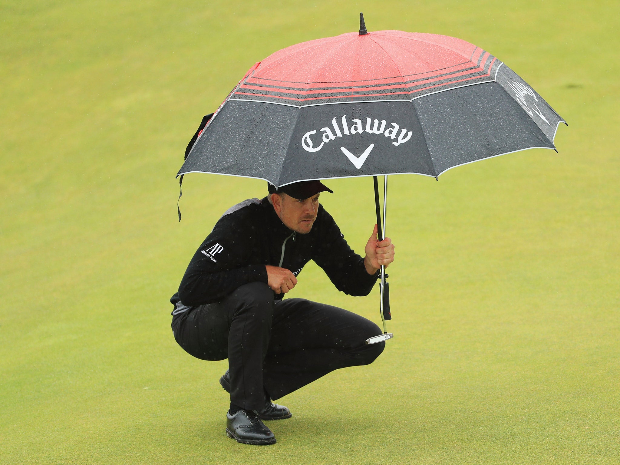 Henrik Stenson takes shelter from the rain as he lines up a birdie putt attempt