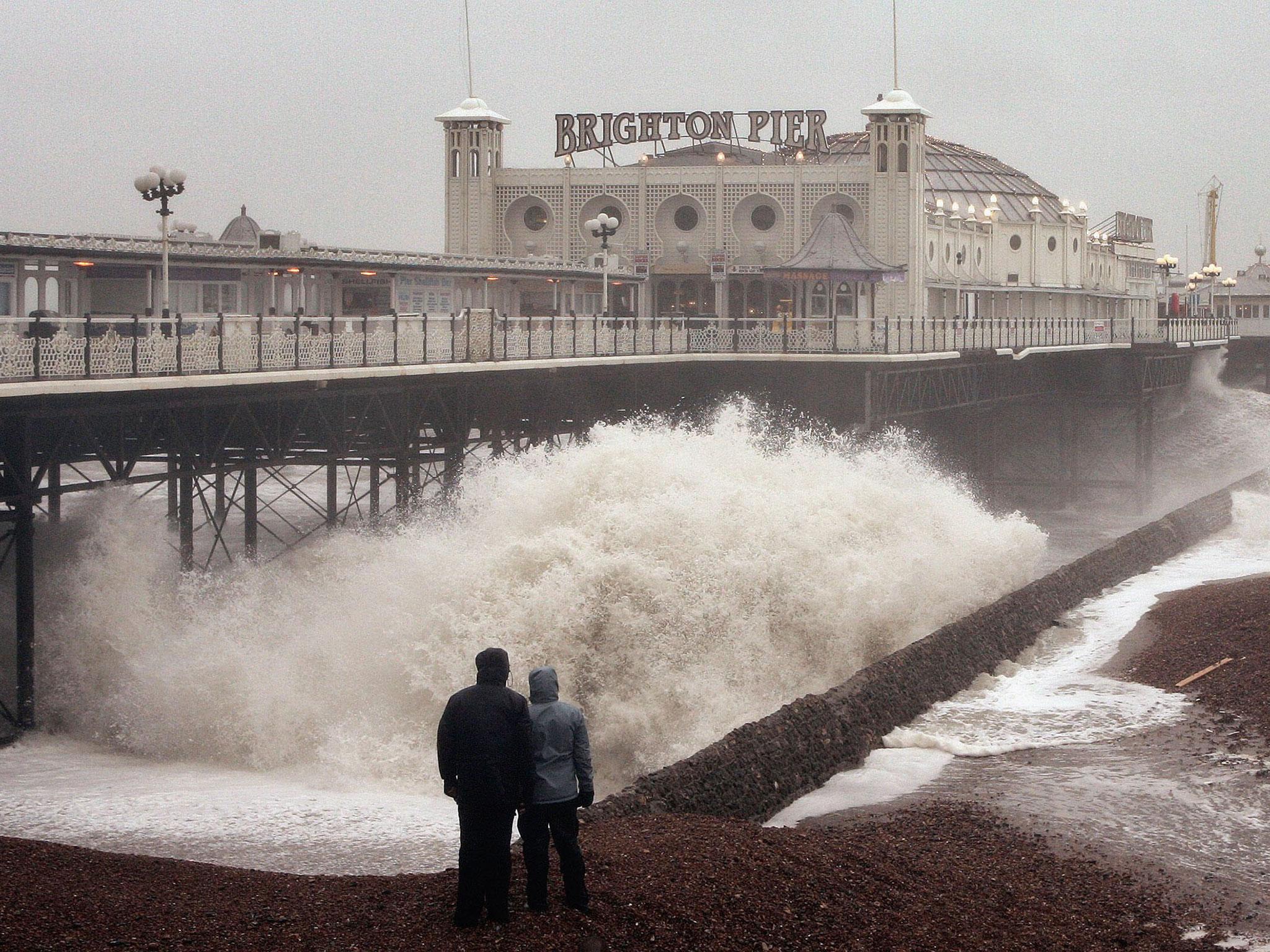 A couple watch as waves crash onto the beach near Palace Pier, which can look bleak on wintry day.