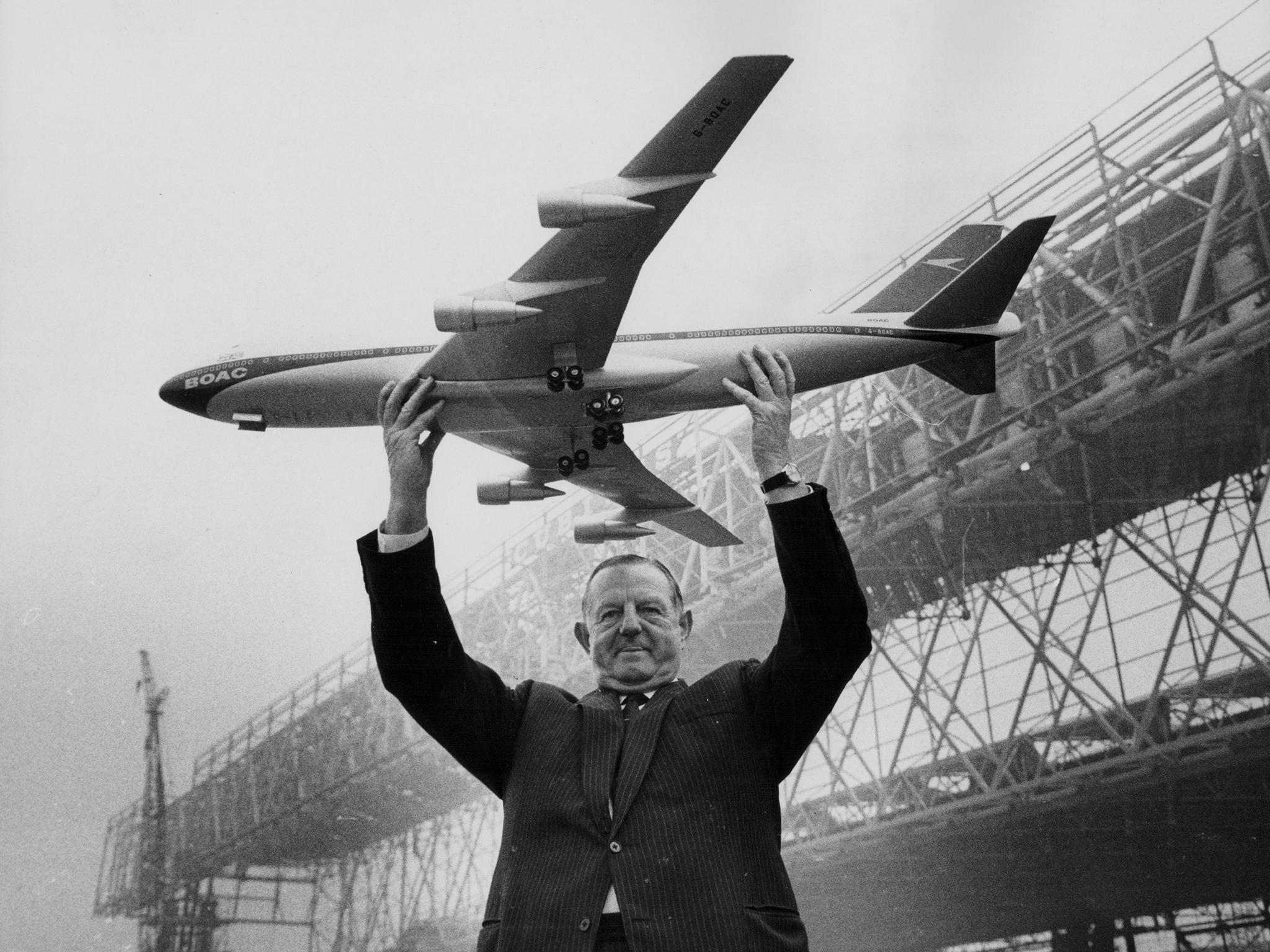 Keith Granville, Managing Director of BOAC, holding up a model of the Boeing 747 jet, with the new aircraft hangars under construction in the background, Heathrow Airport, London, March 17th 1969