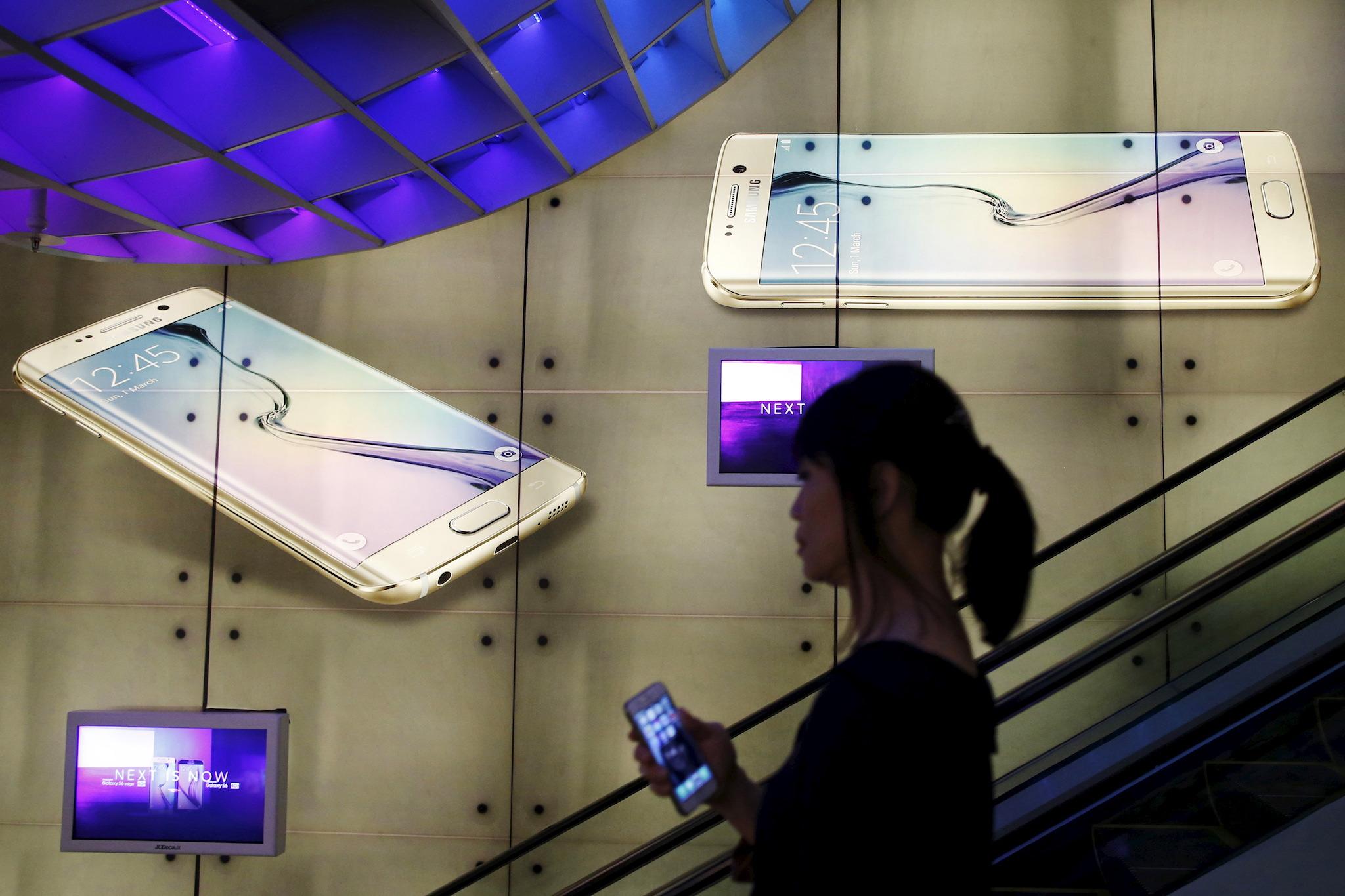 A woman holding an Apple iPhone passes a Samsung Galaxy S6 advertisement at a mall in Singapore April 24, 2015