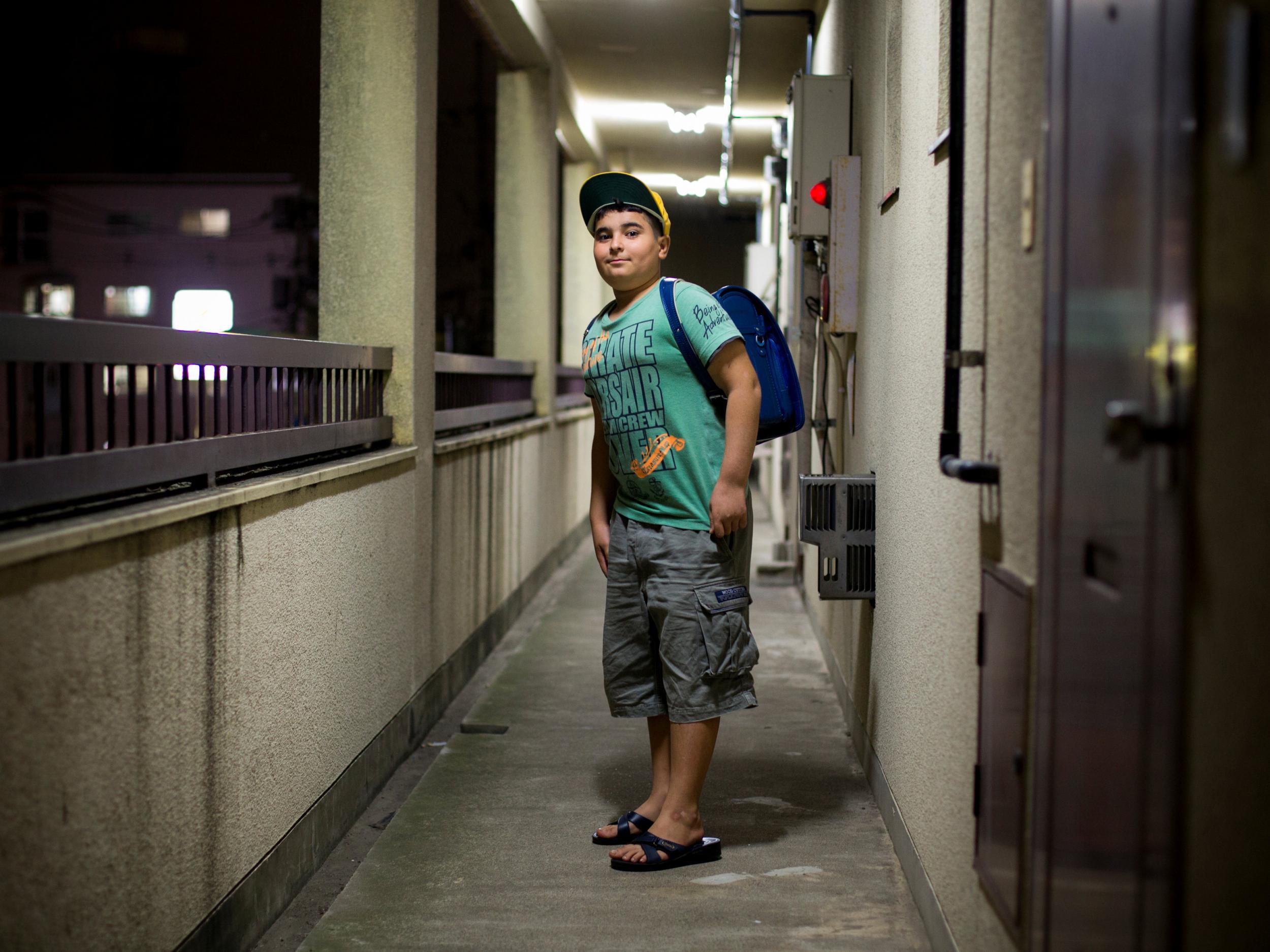 Kurdish boy Ozgur Cinaroglu, 12, poses with this school rucksack outside his house in Warabi