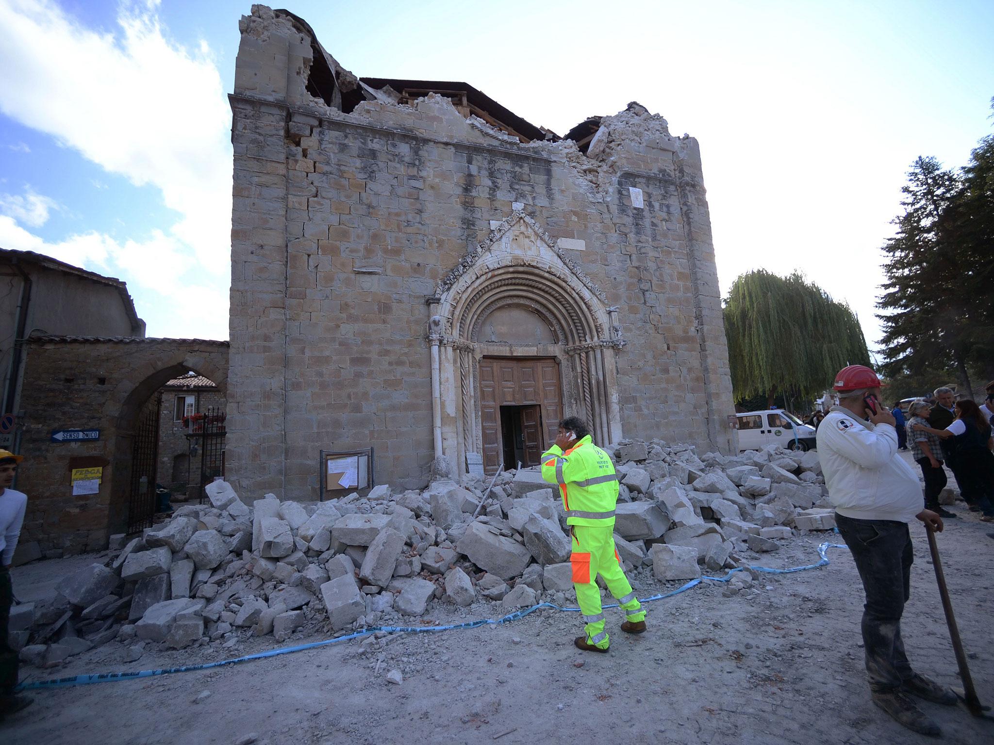 People stand in front of a damaged church in Amatrice