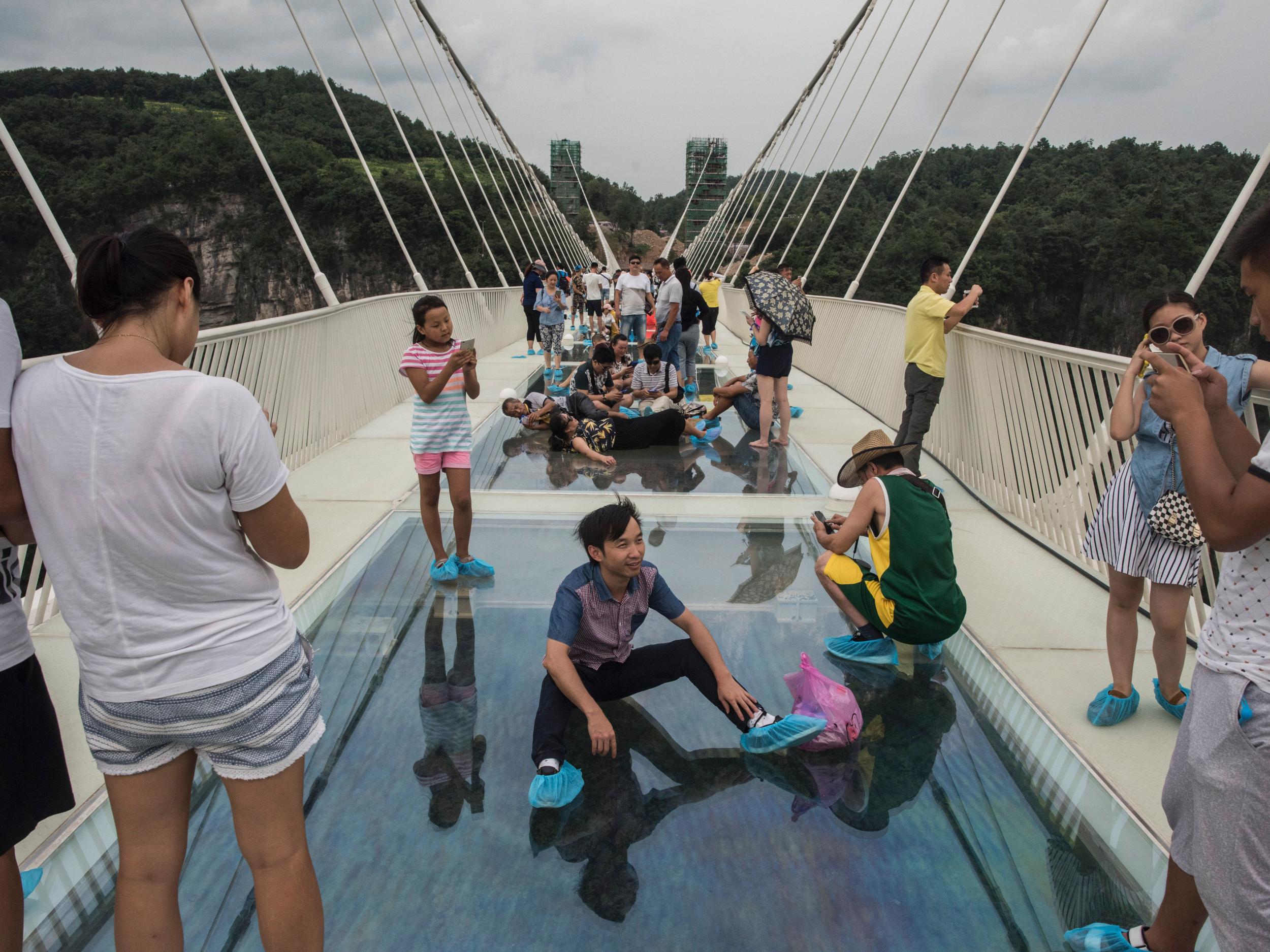 A tourist poses for a photograph on the world's highest and longest glass-bottomed bridge