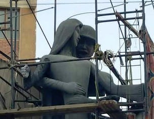 A sculpture, titled 'Mother of the Martyr', depicts a slender peasant woman, a traditional artistic representation of Egypt, with her arms outstretched with a helmeted soldier standing behind her, at a public square in Sohag, Egypt