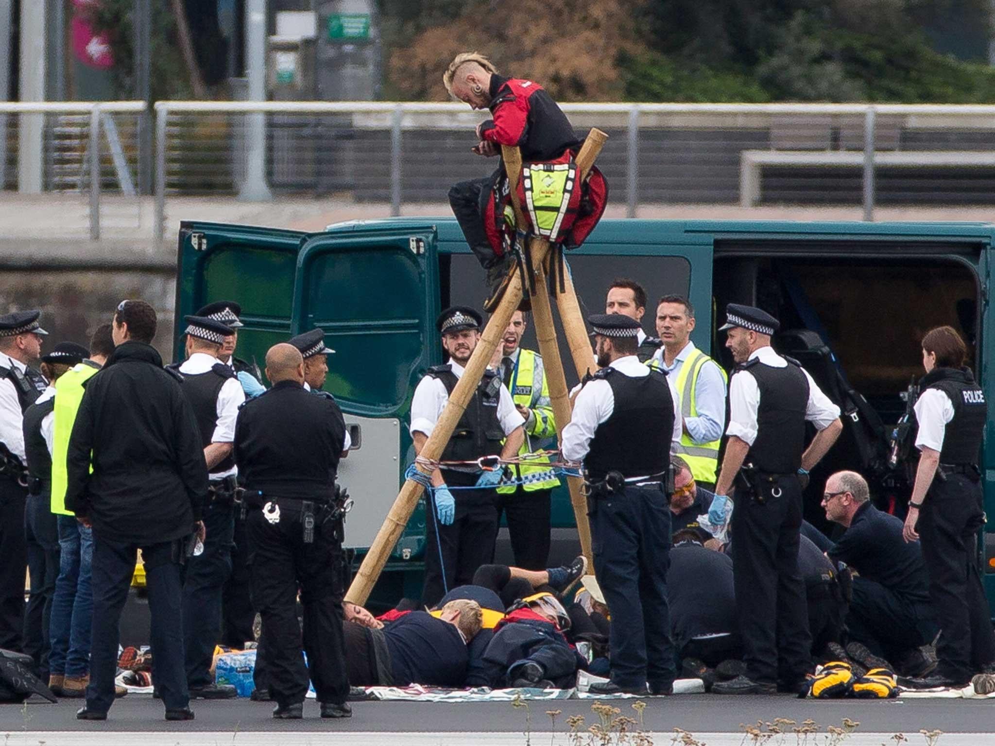 Emergency services surround BLM protesters after they locked themselves to a tripod on the runway