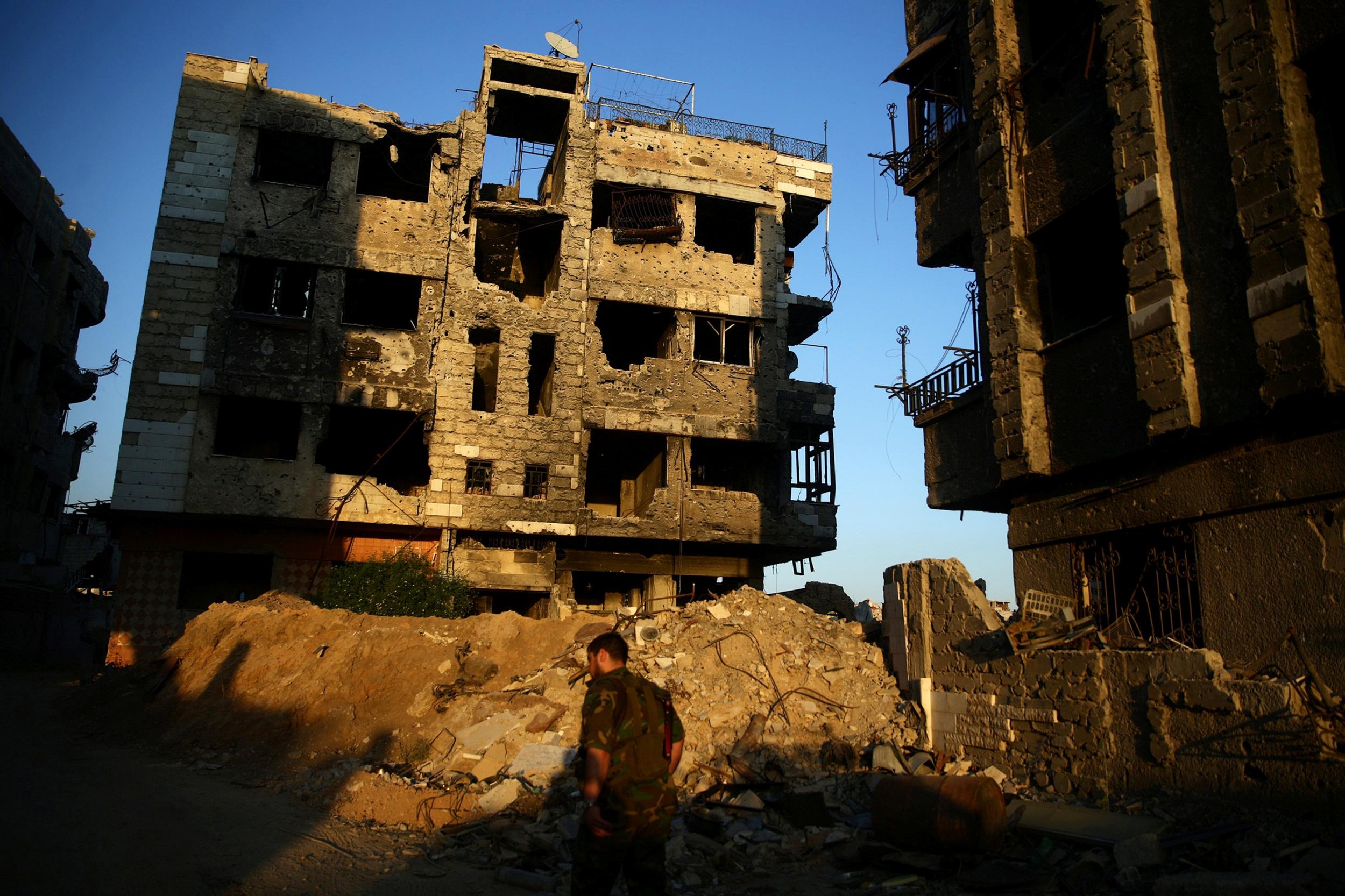 A fighter from the Free Syrian Army's Al Rahman legion walks past damaged buildings in rebel-held Jobar district of Damascus