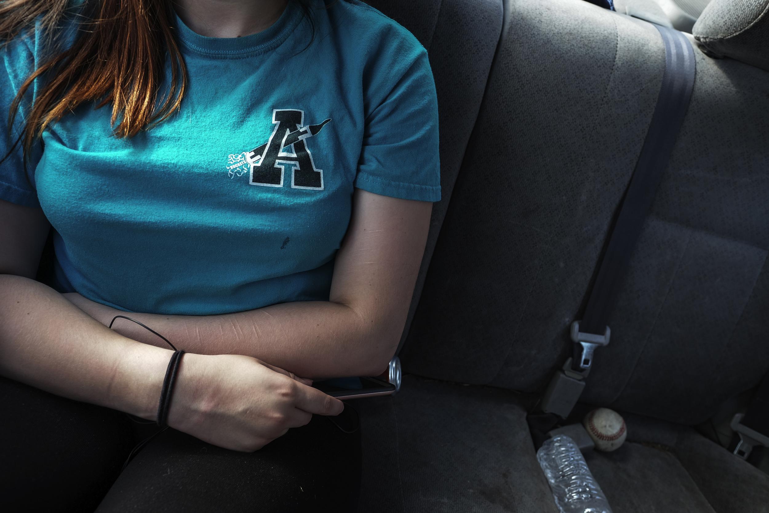 Maureen rides in the back of her father's car. The scars from when she cut herself are still visible on her arms.