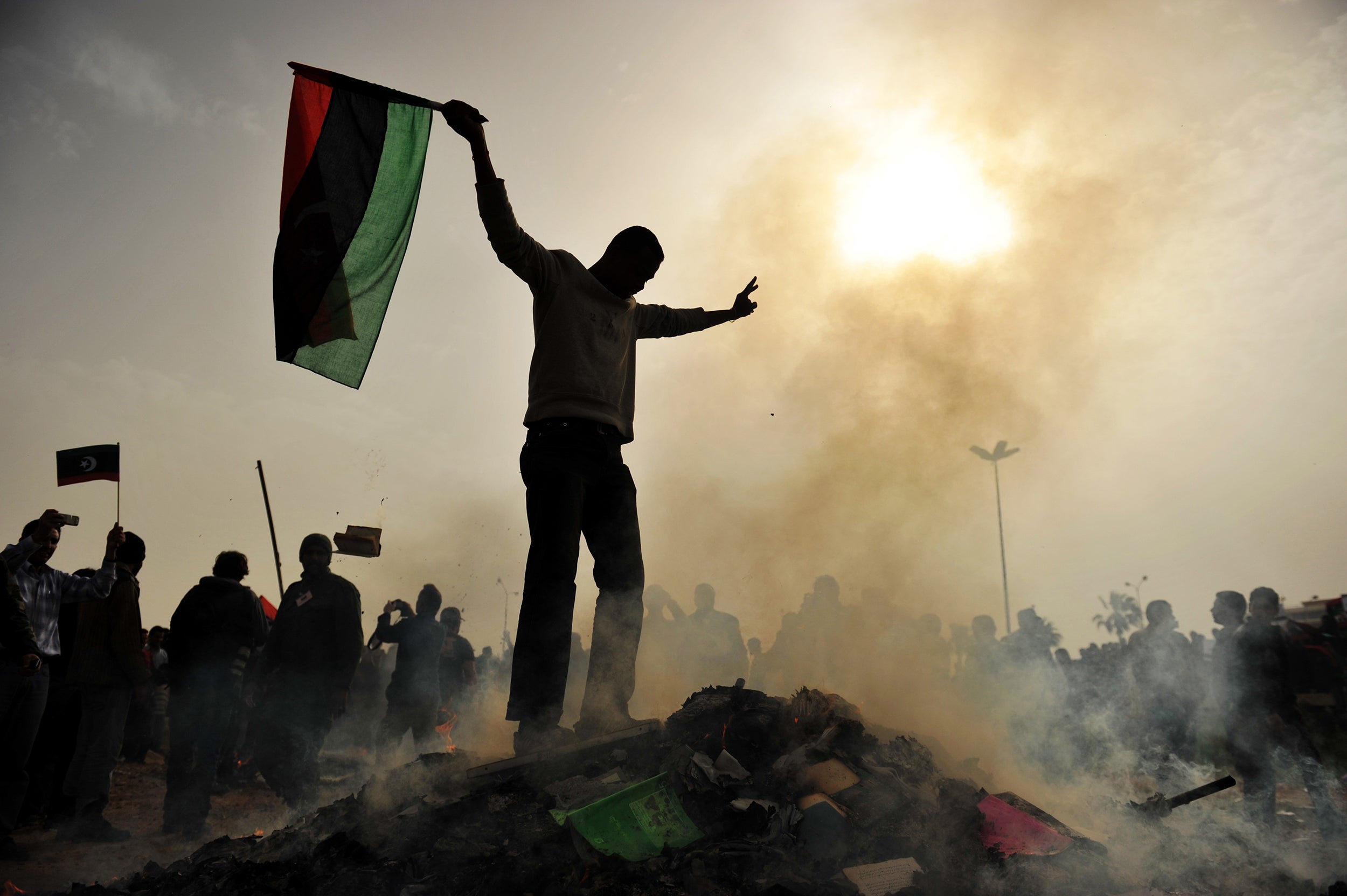 A resident of Benghazi stands atop a burning heap of books authored by Gaddafi