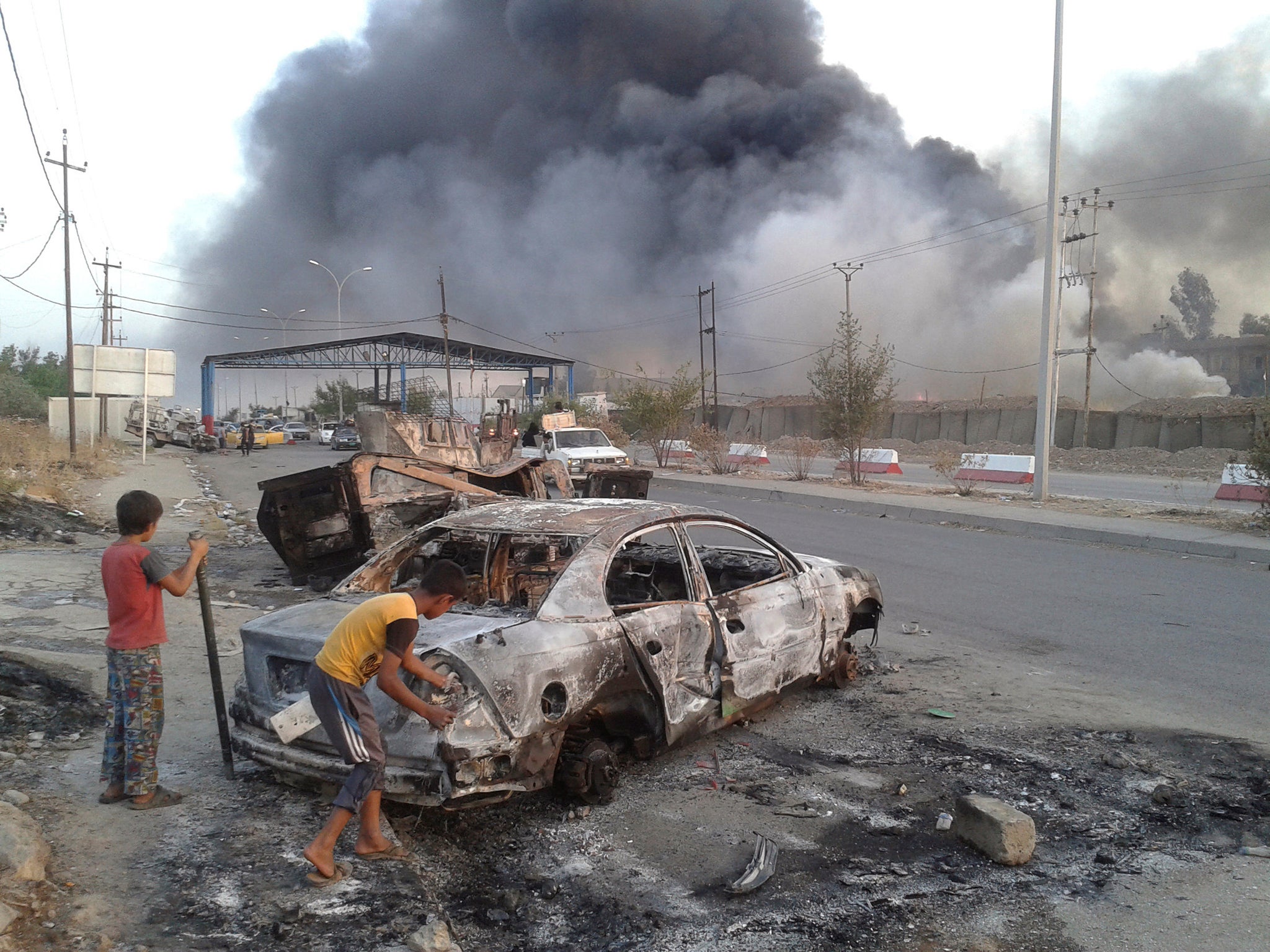 Civilian children stand next to a burnt vehicle during clashes between Iraqi security forces and Islamic State in Mosul, Iraq