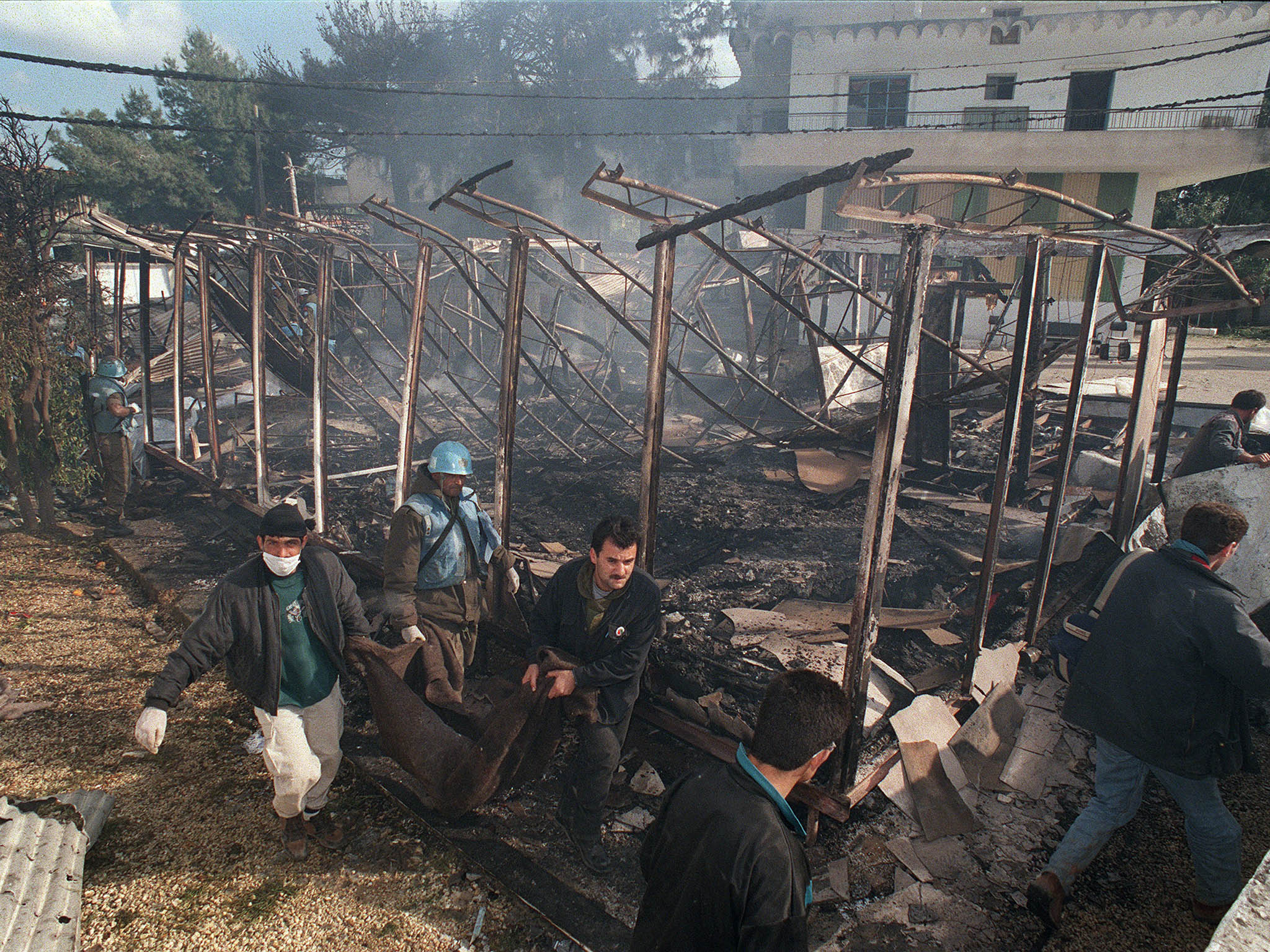 A UN soldier and civilians remove the body of a victim of Israeli shelling in Qana, Lebanon, in April 1996