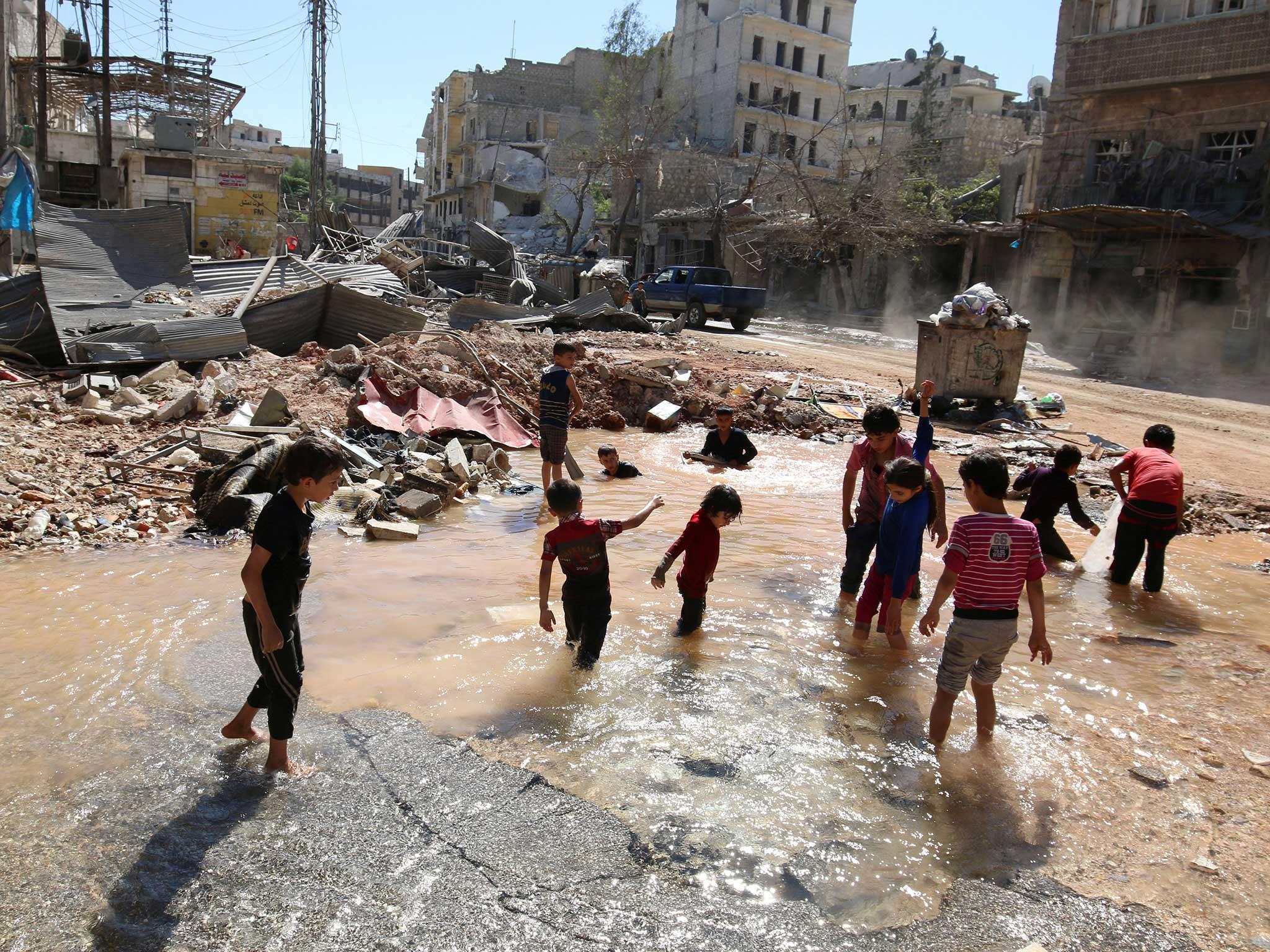 Children play in water from a burst pipe in the rubble of Aleppo