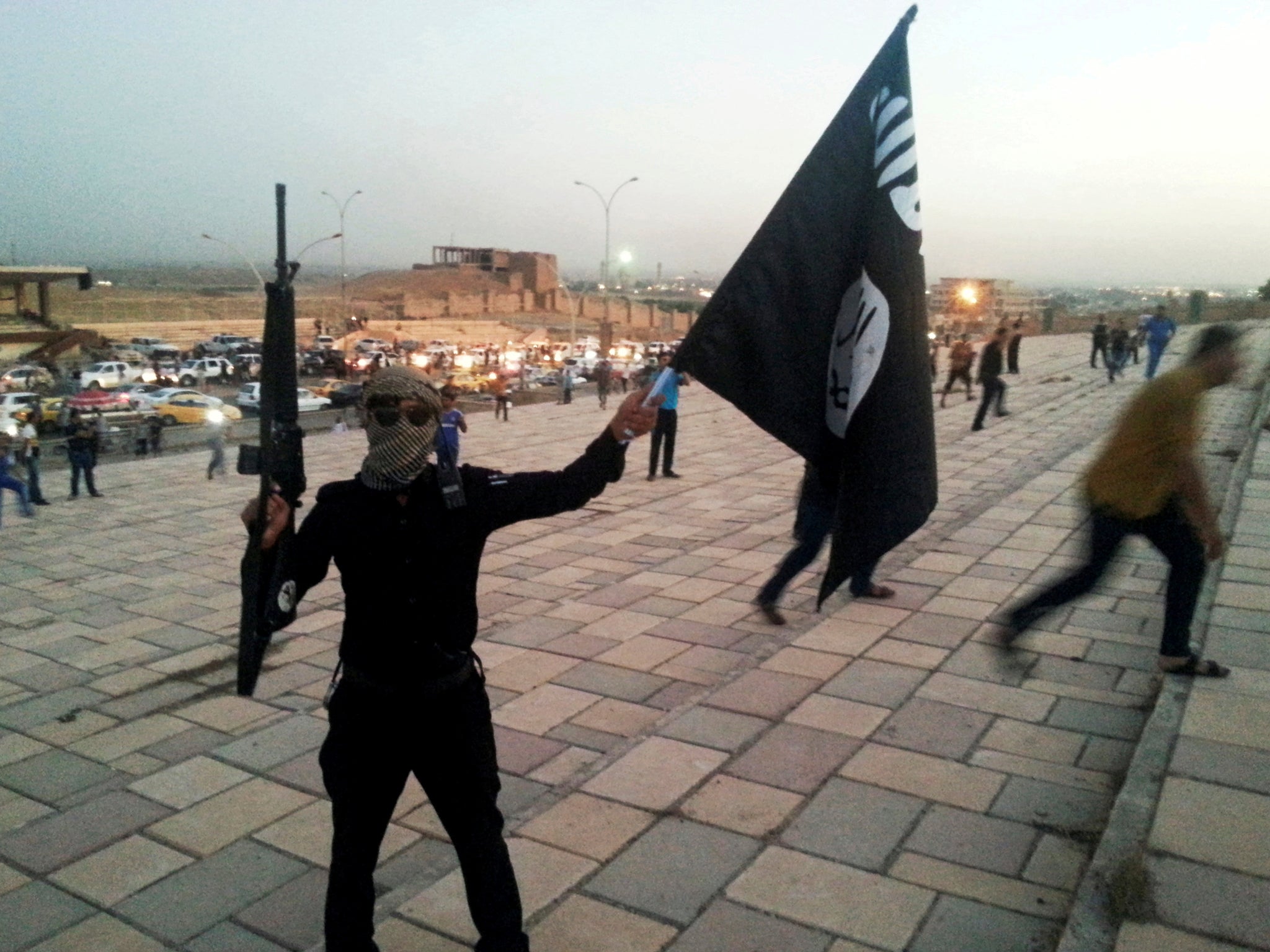 An Isis fighter brandishes a flag and automatic rifle on a street in Mosul